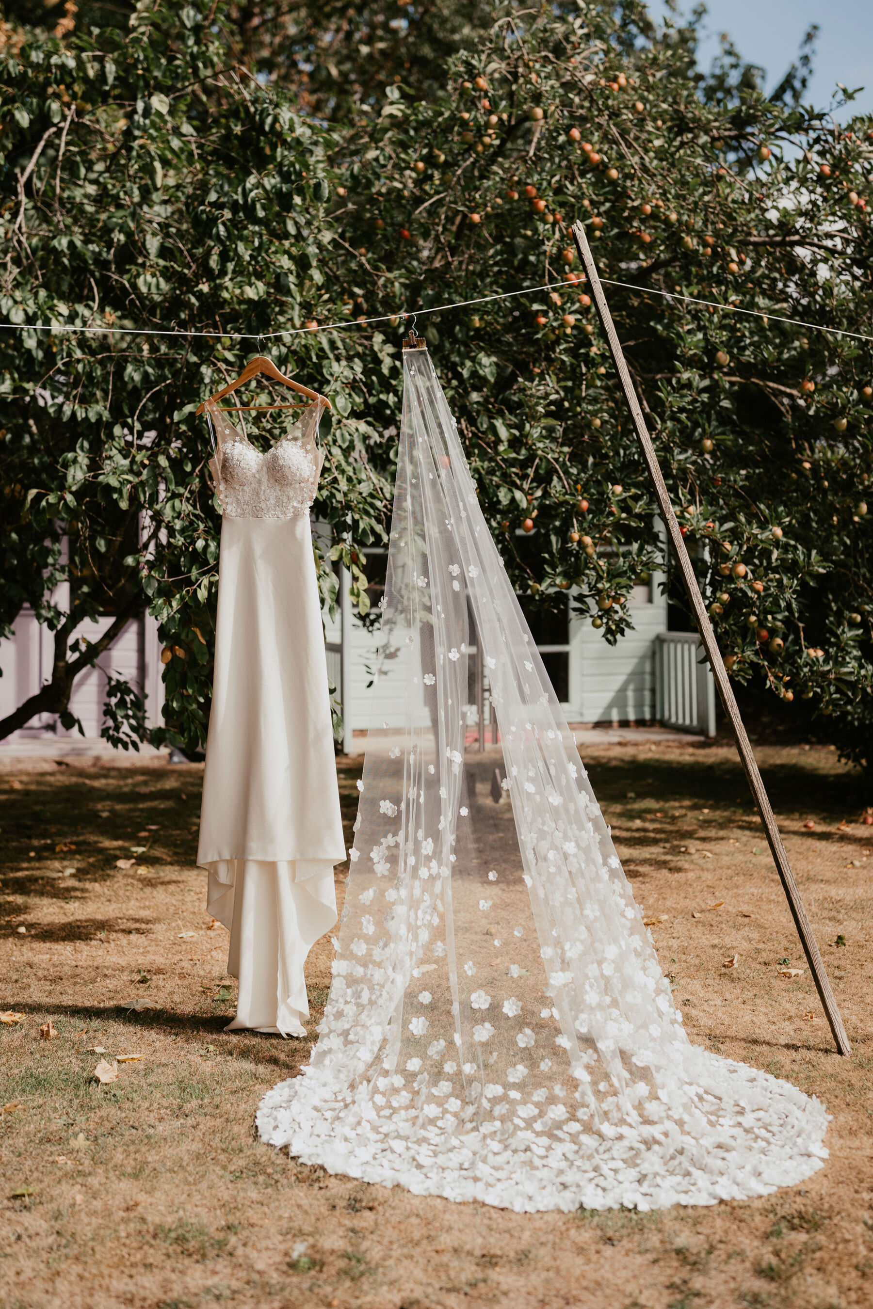 Wedding dress and veil hanging on a washing line. Veil is covered in hundreds of cut-out fabric flowers.