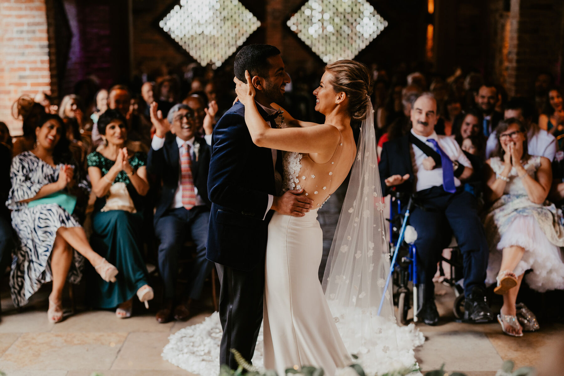 Bride and groom embracing inside Shustoke Barn wedding venue, Warwickshire. Groom in navy blue tuxedo, bride in dress she made herself - Unveiled by Sophie.