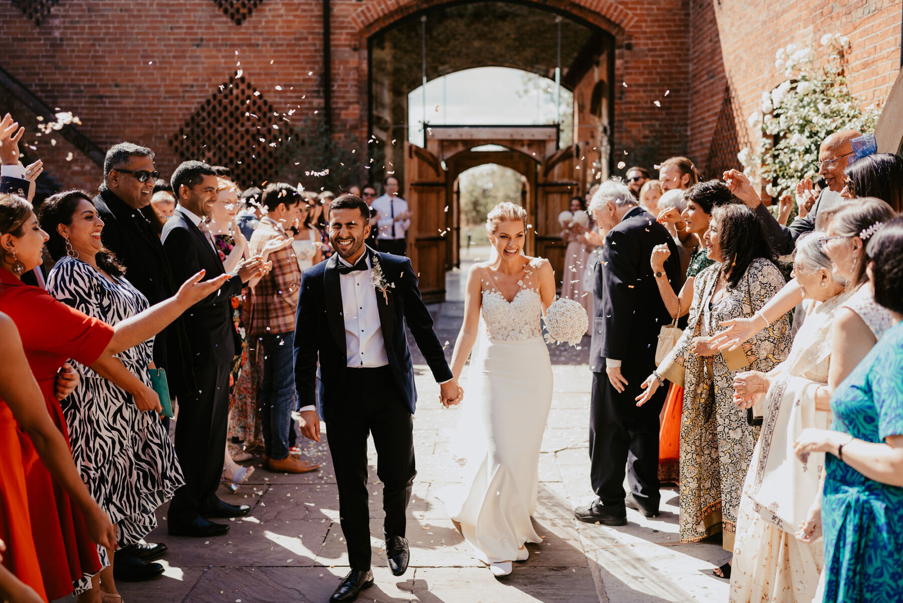 Mixed race bride and groom in a shower of confetti at Shustoke barn wedding venue.