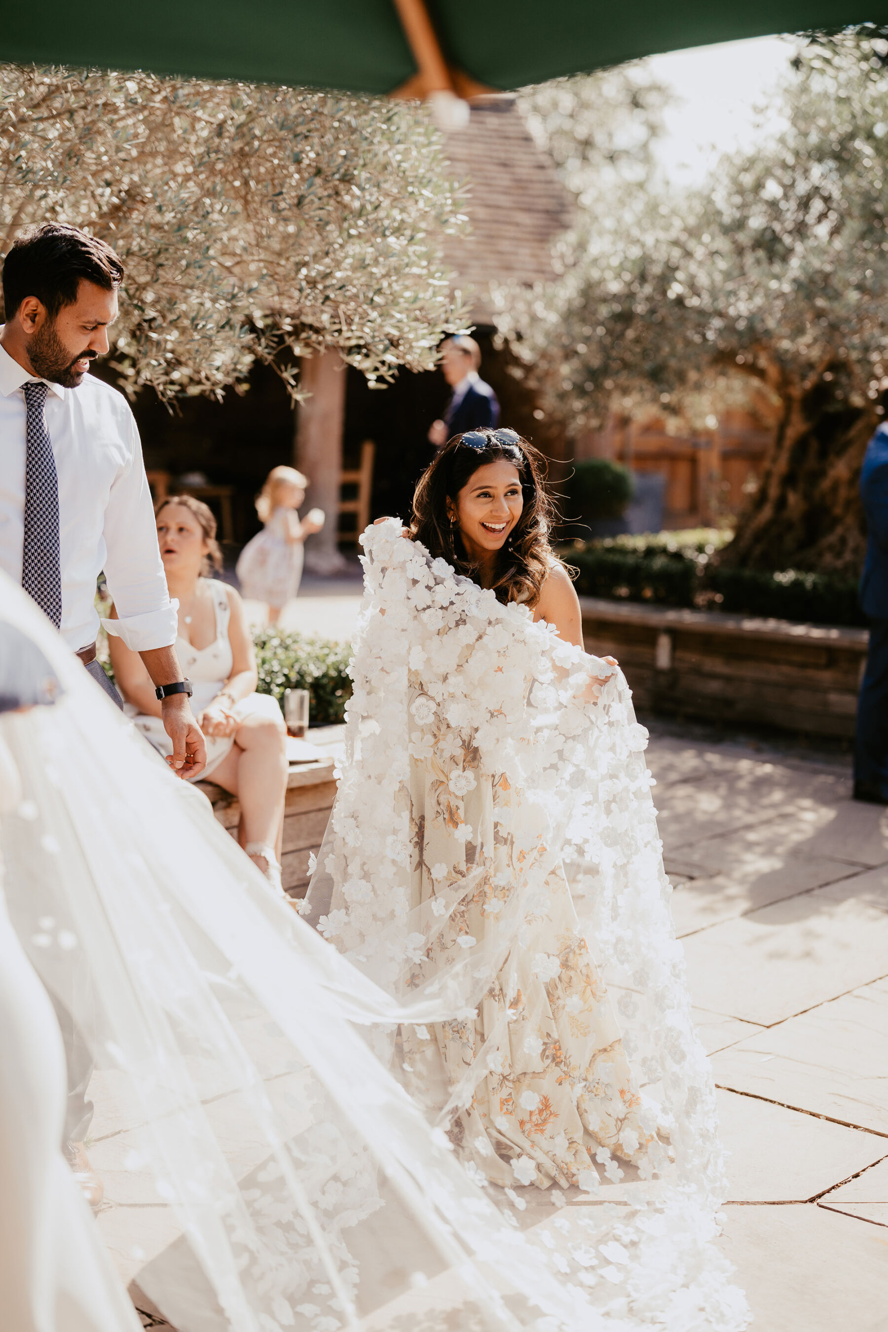 Wedding guest gathering the end of the bride's long wedding veil covered in silk flowers and petals.