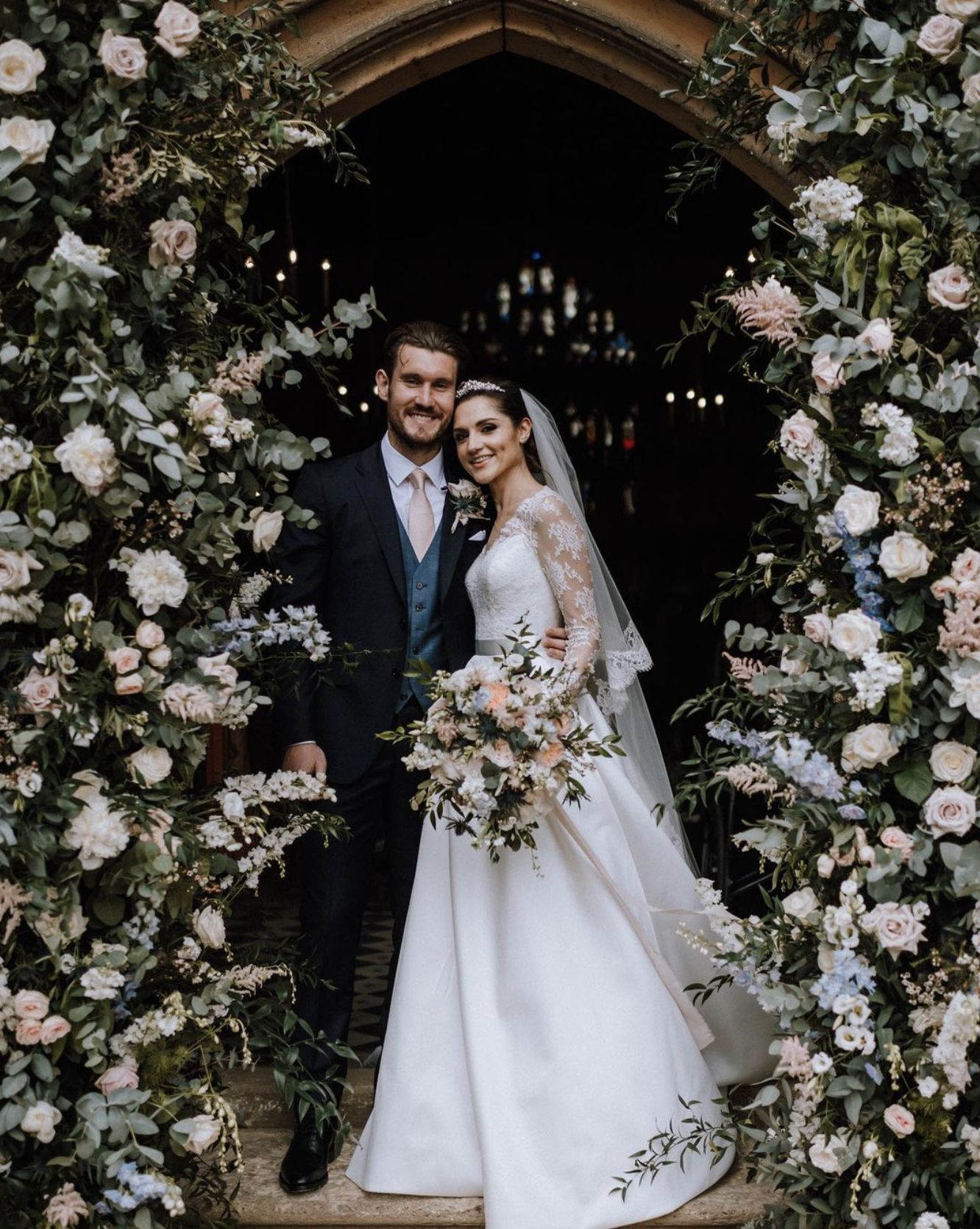 Eucalyptus Events, Cotswolds Wedding Planner - Beautiful floral arch surrounding a church door with bride and groom standing in the middle. 
