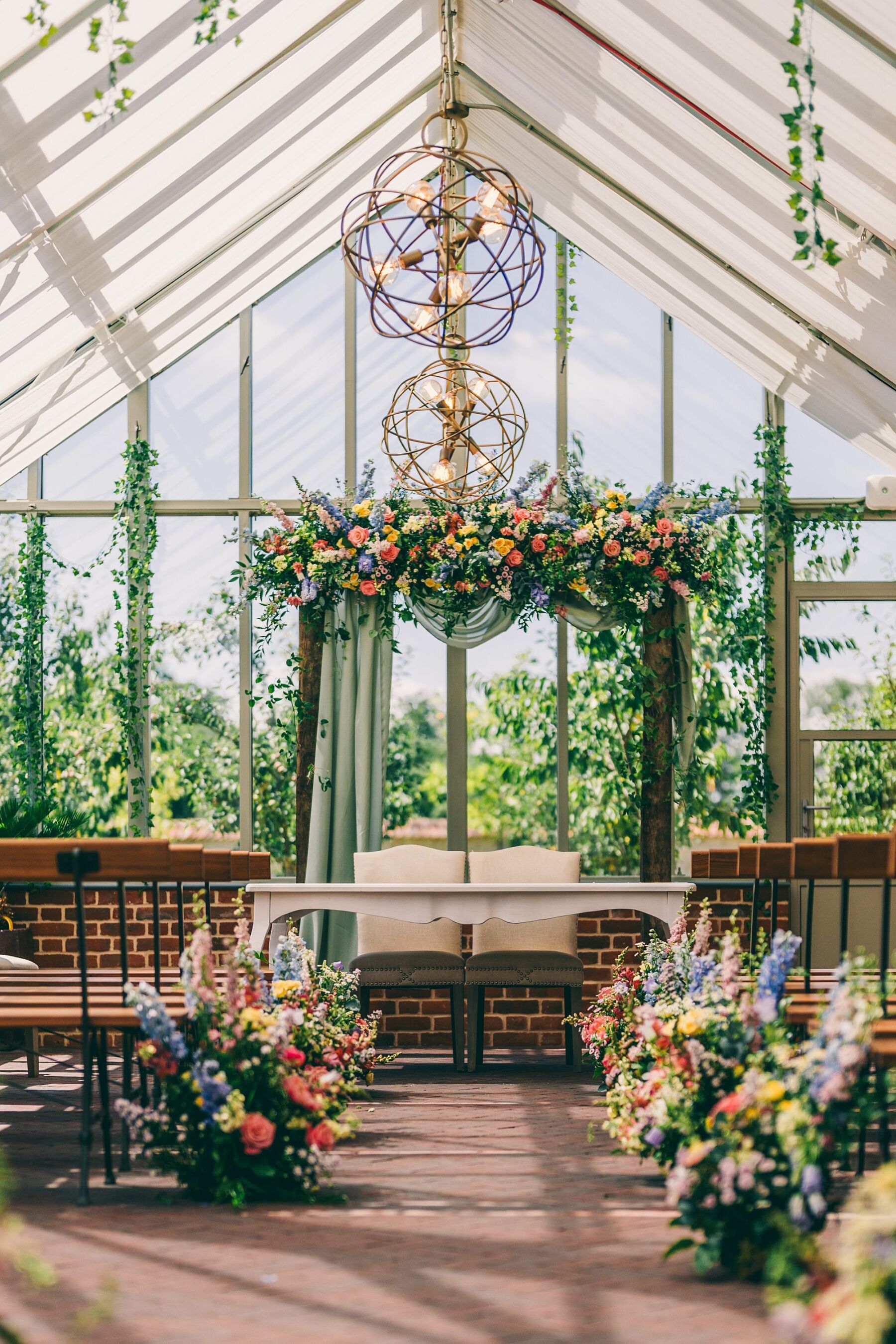 Eucalyptus Events, Cotswolds Wedding Planner. Bright and colourful flowers hanging over a wedding reception registrars table and lining the aisle.