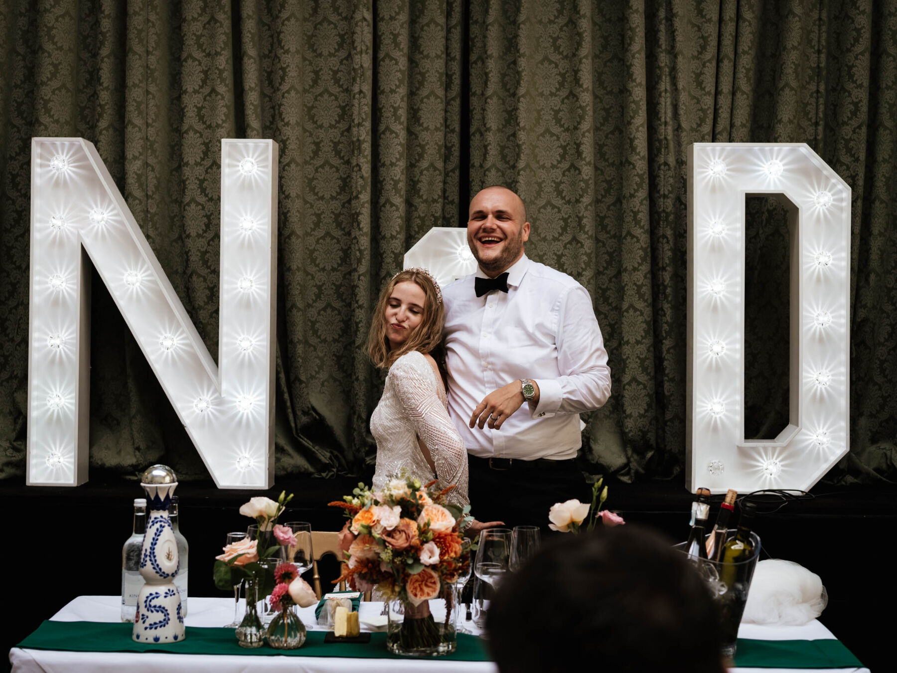 Couple giggling by large wedding lights. Robin Goodlad Photogarphy.