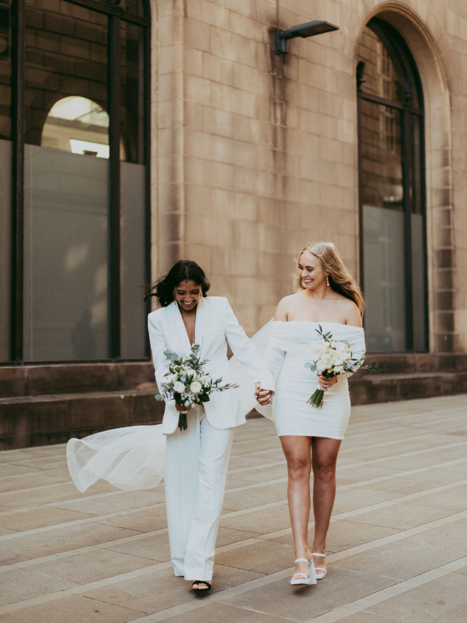 Lesbian bride in a suit holding hands with her Lesbian bride in a short dress and long veil. Daniel Mice Photography.
