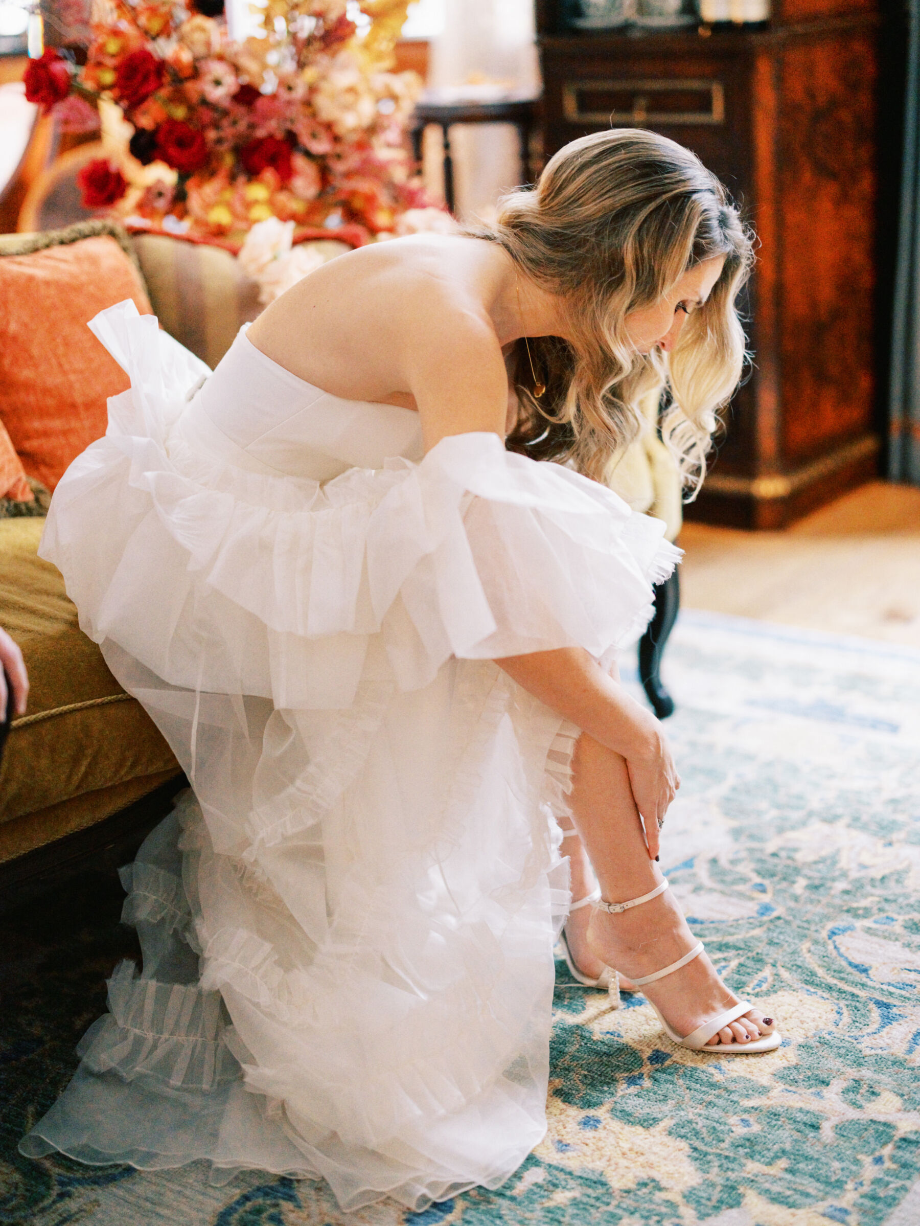 Bride bending forward in her chair to put on her wedding shoes. Halfpenny London dress. Kernwell Photography.