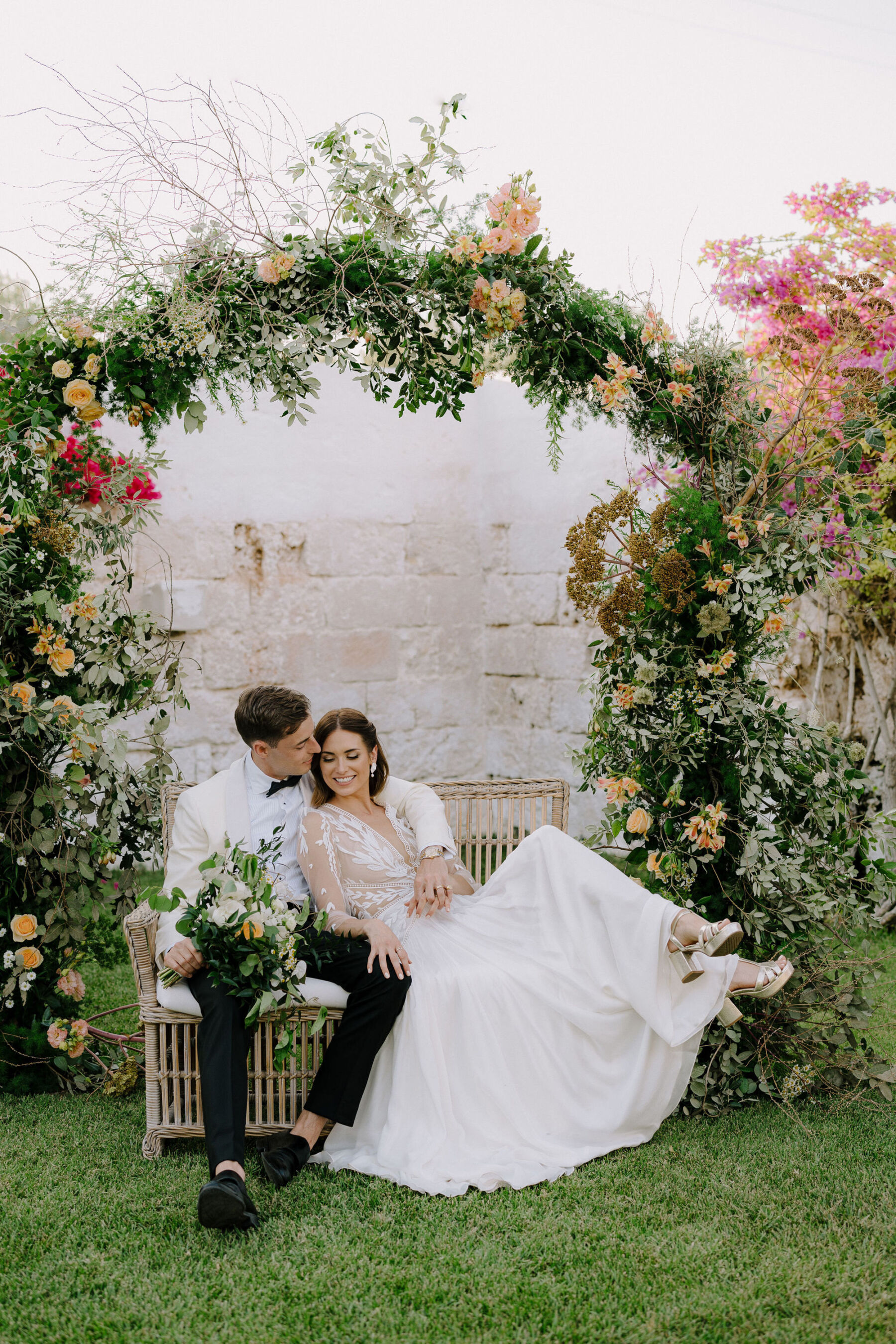 Italian villa weding. Bride and groom sitting under a floral arch in a romantic embrace.