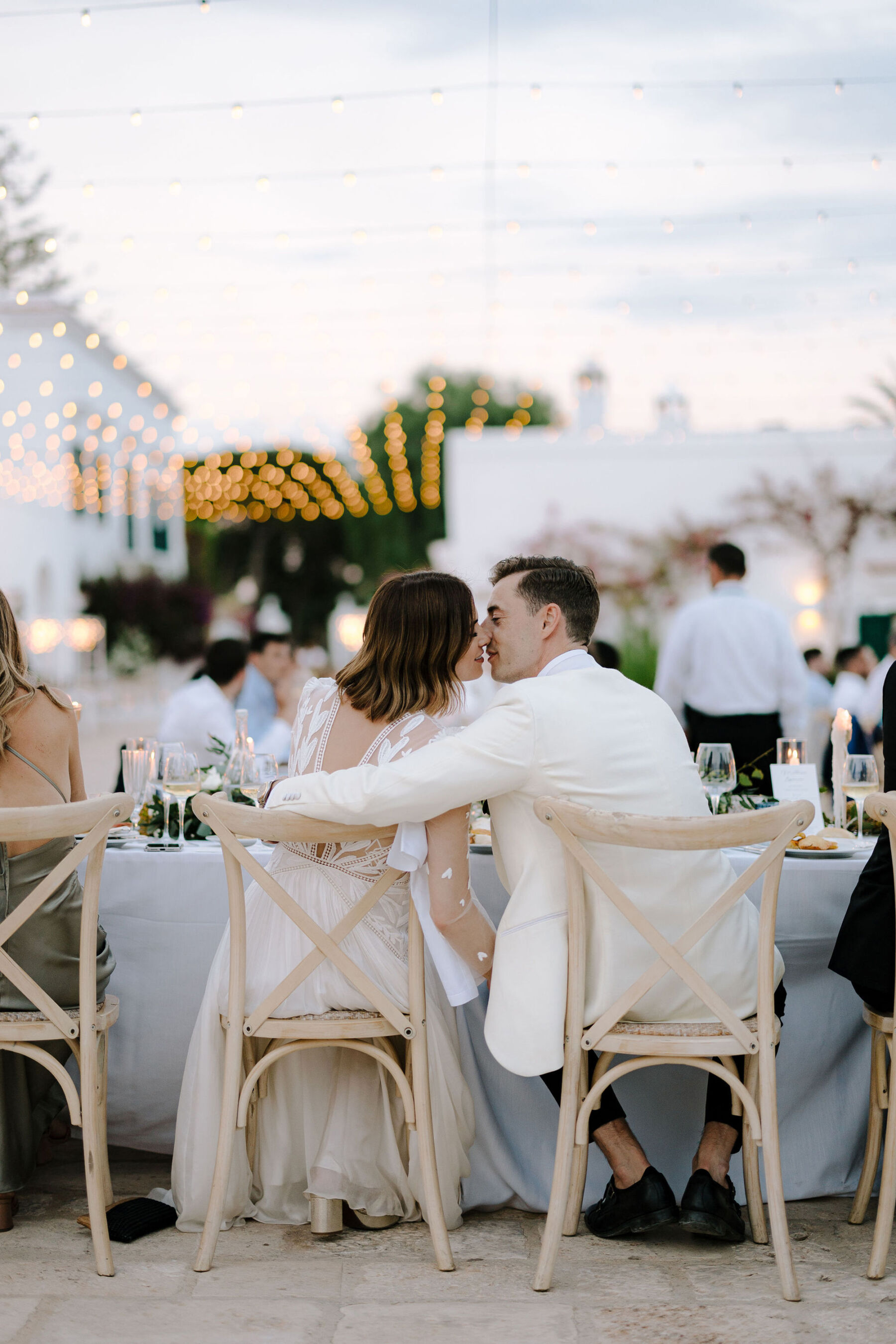 Bride and groom sitting on lime wash cross back chairs at an Italian villa wedding.
