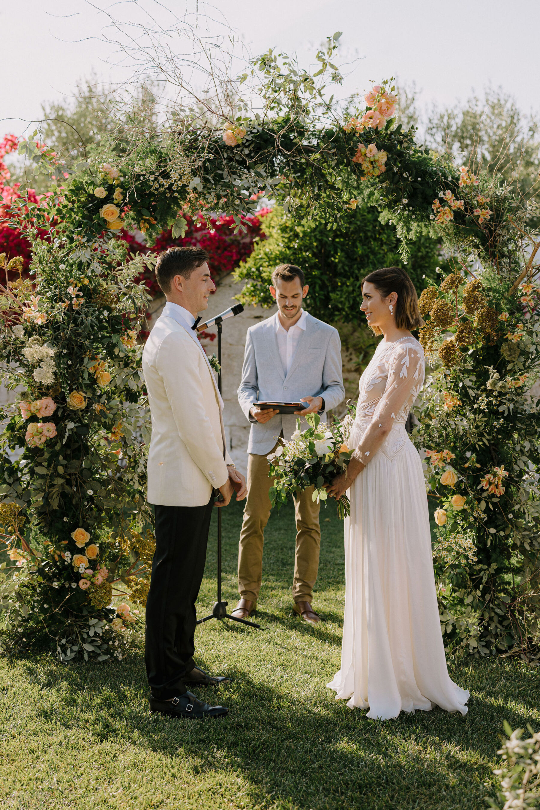 Bride and groom in an outdoor wedding ceremony at an Italian villa, standing by a natural and undone floral arch.