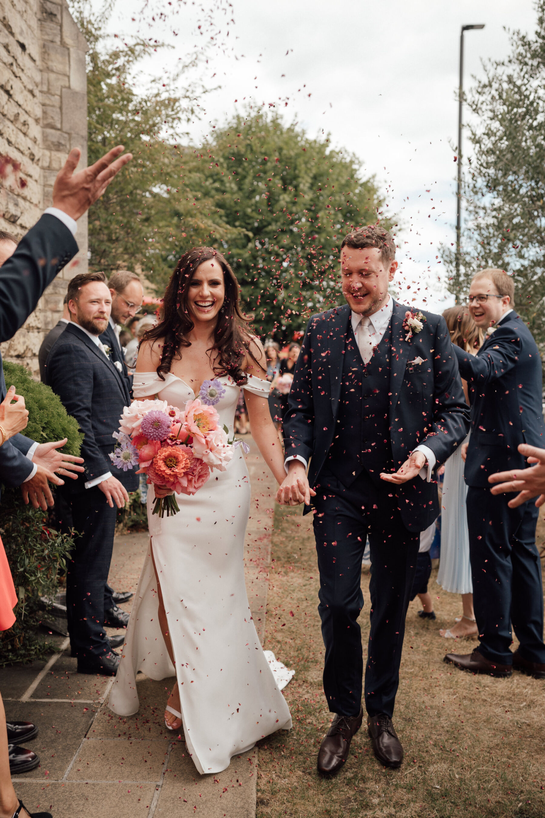 Bride and groom in a confetti shower. Bride in Roxy by Suzanne Neville, carrying a large, bright and bold bouquet by BUD Flora. The Shannons Phtoography.
