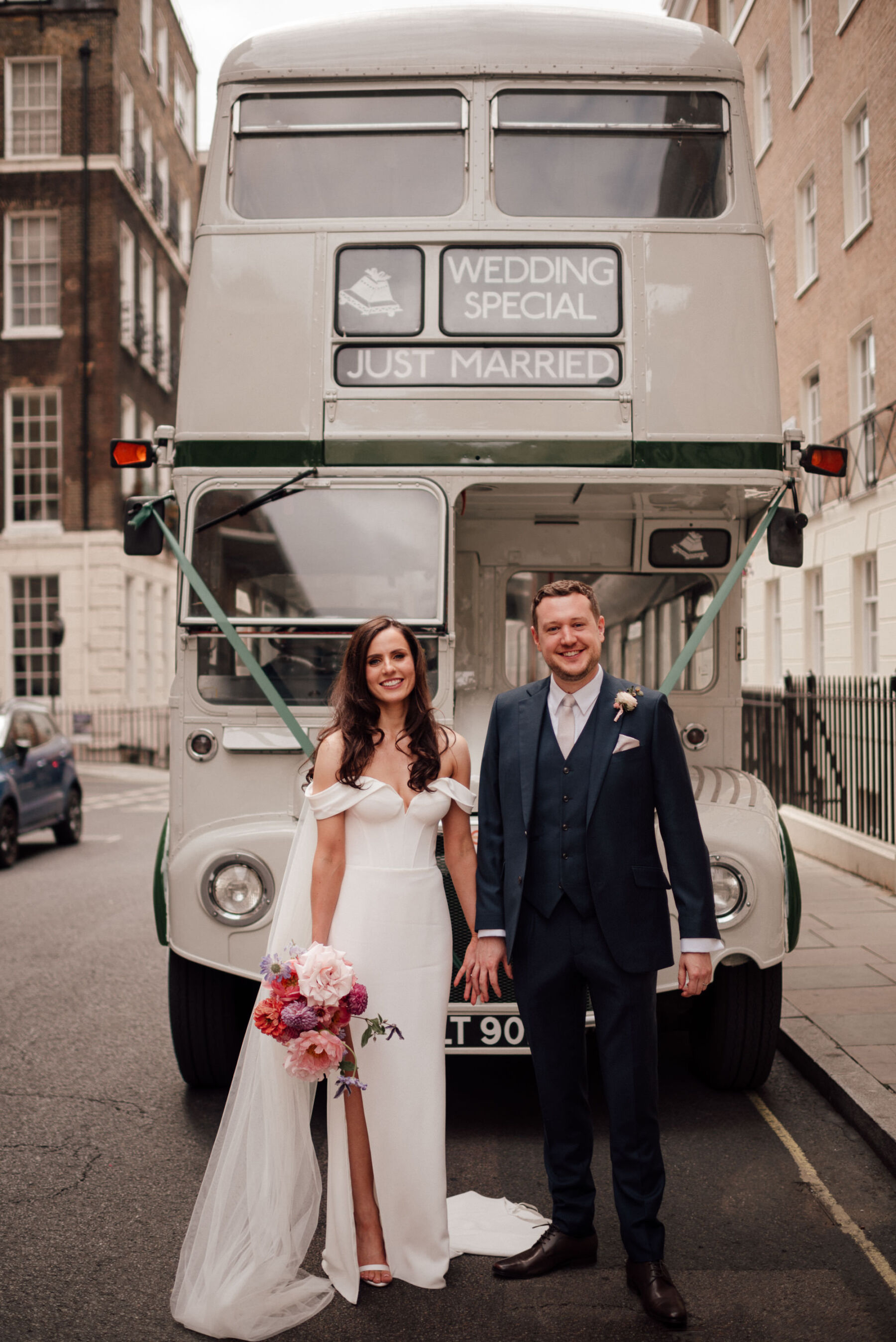 Bride and groom standing by a white Routemaster wedding bus. The Shannons Photography.