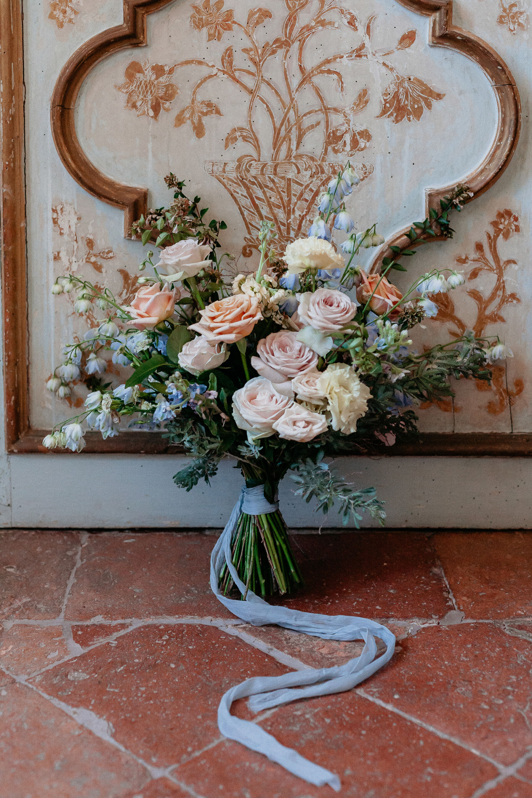 Bouquet of romantic cream, peach and pale pastel wedding flowers with silk blue ribbon.
