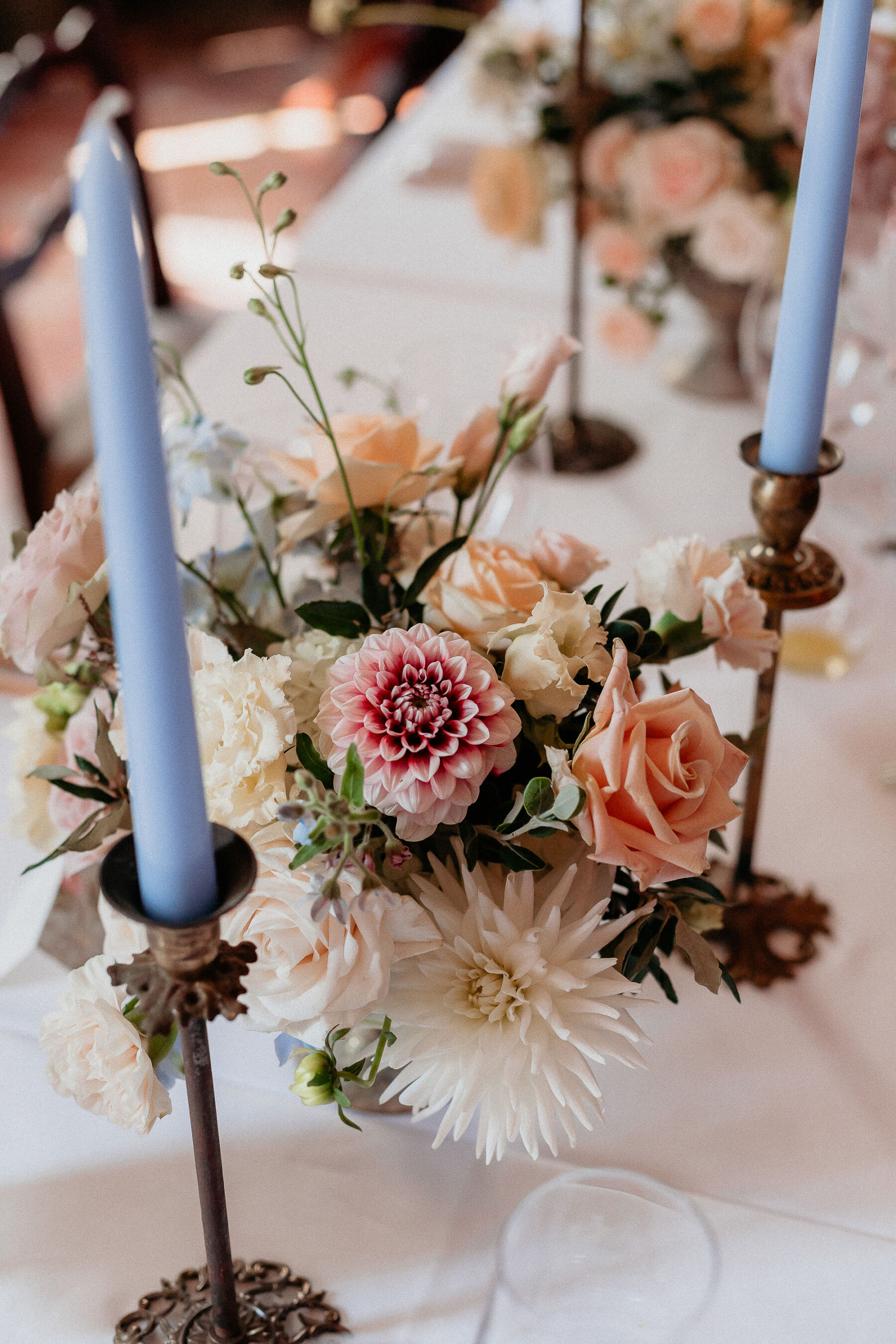 Romantic cream, peach and pale pastel wedding flowers with tall blue taper candles. Italian wedding.