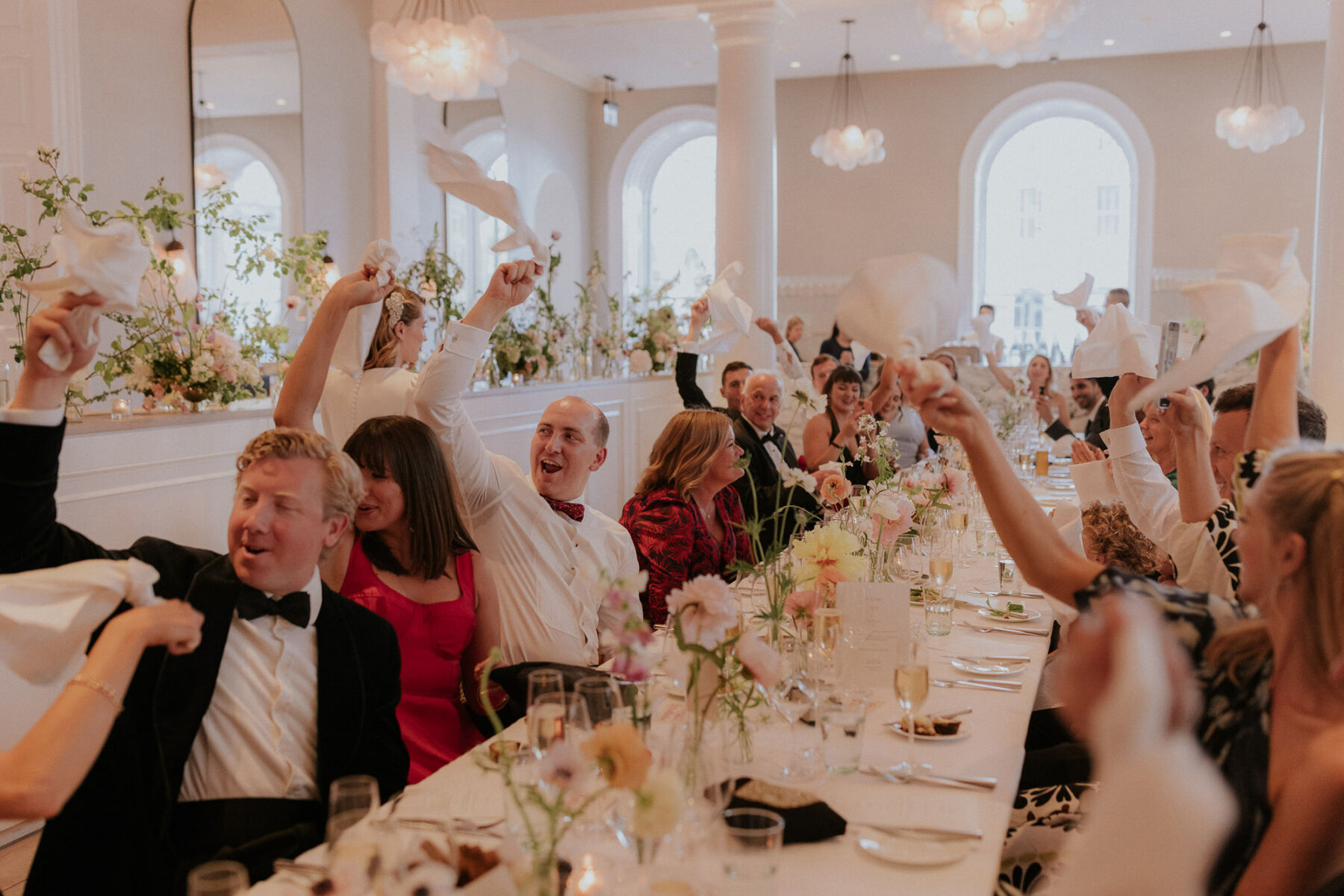 Guests waving napkins at wedding reception at Spring restaurant, London. Elegant flowers in bud vases on the table. Maja Tsolo Photography.