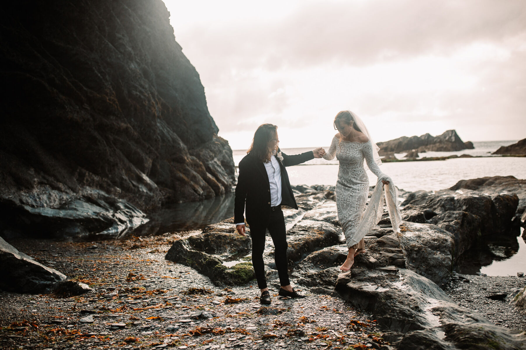 Bride and groom walking across the beach at Tunnels Beaches wedding venue in Devon. Bride wears Grace Loves Lace.