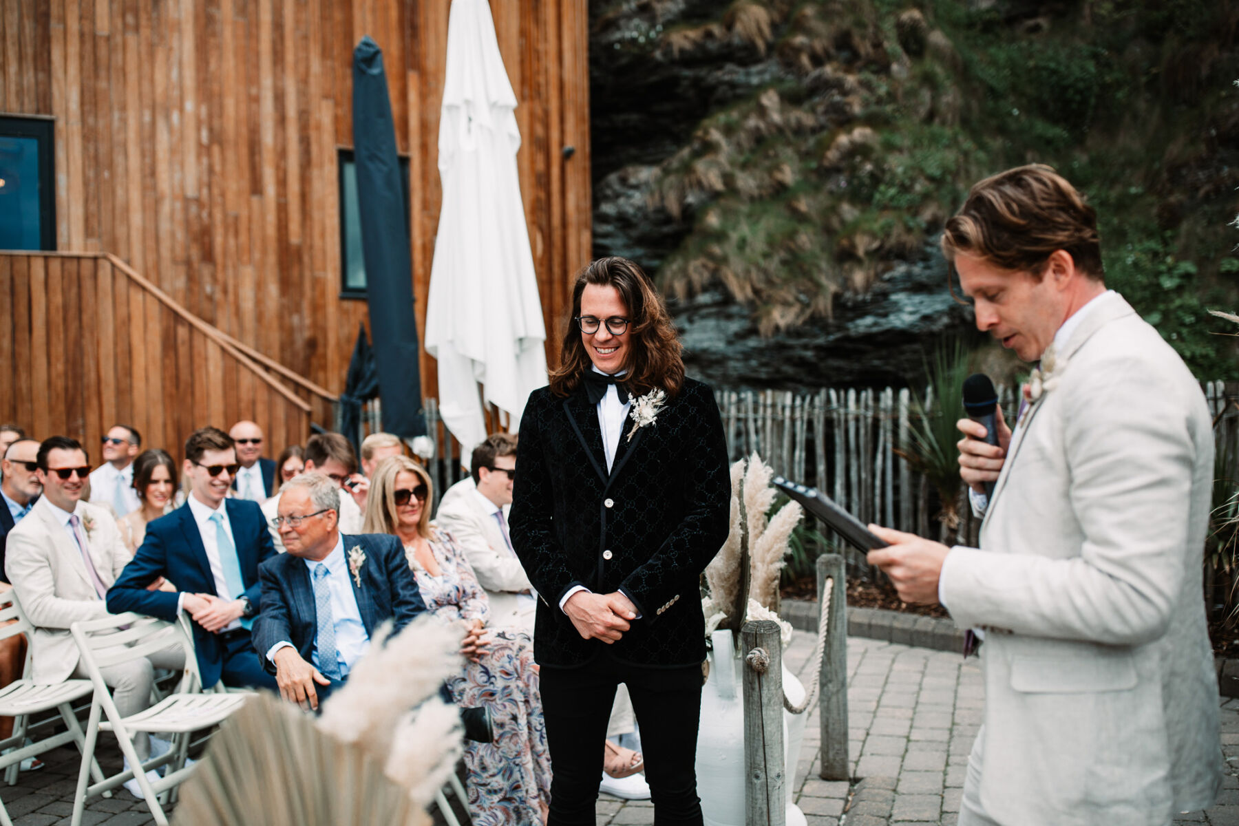 A Devon Wedding with a Sea View for Georgie in Grace Loves Lace 20 Groom with long hair and glasses in black tie at Tunnels Beaches wedding venue, Devon