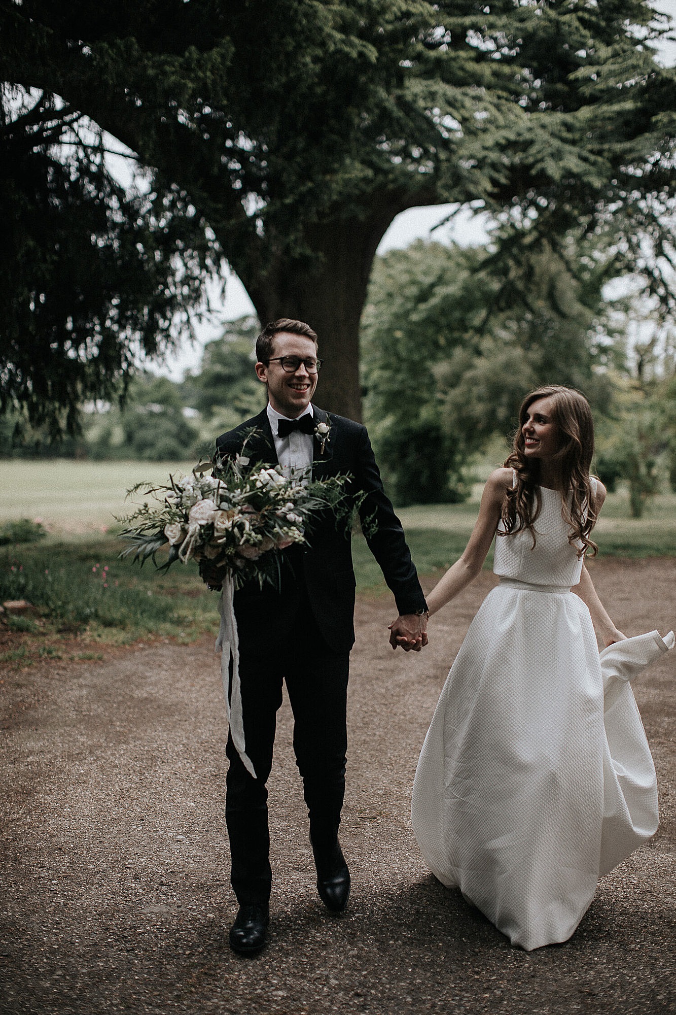 Elegant bride holding hands with groom who is holding a bouquet. Bride wears Jesus Peiro top and skirt.