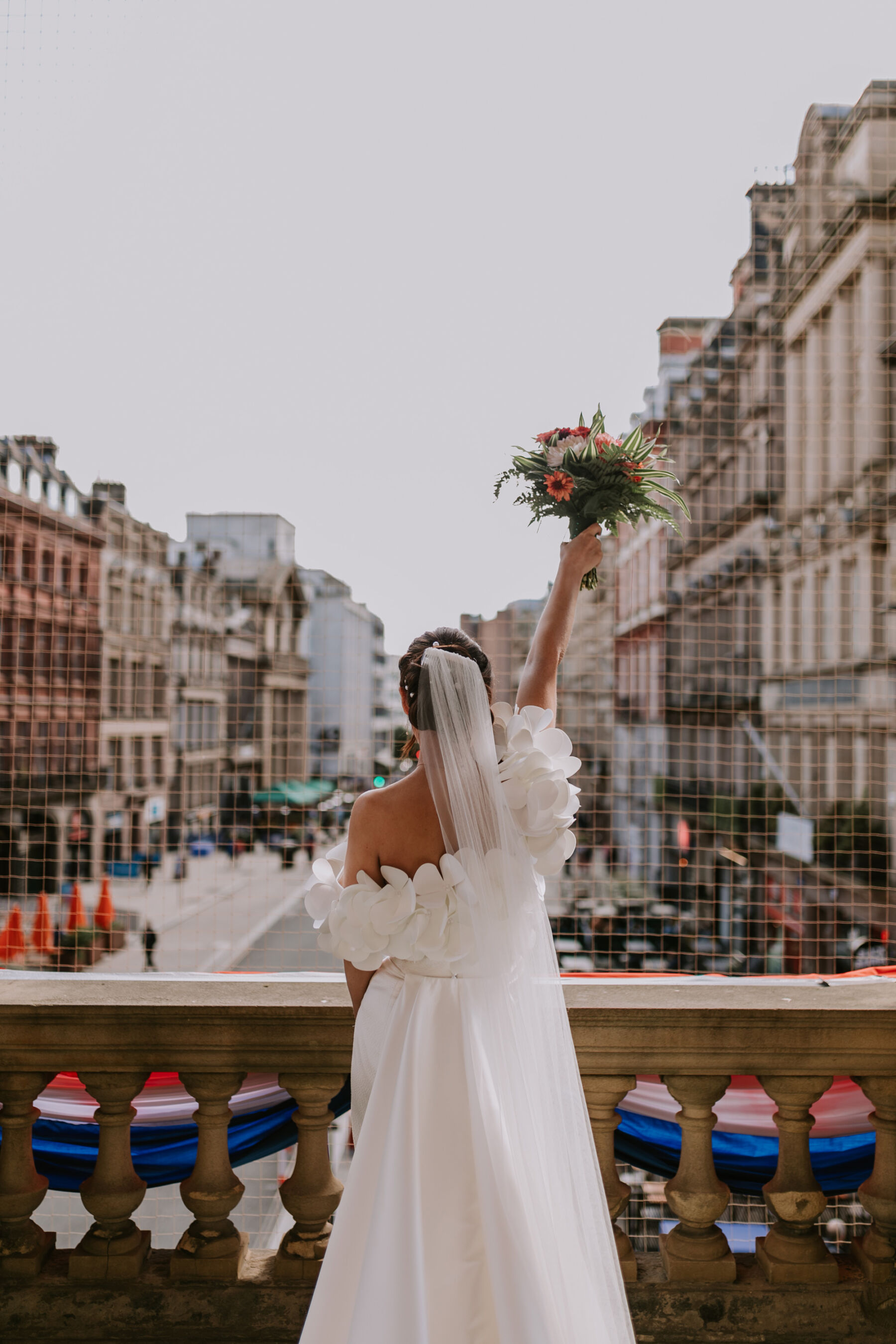 Bride standing on a balcony holding her bouquet up high