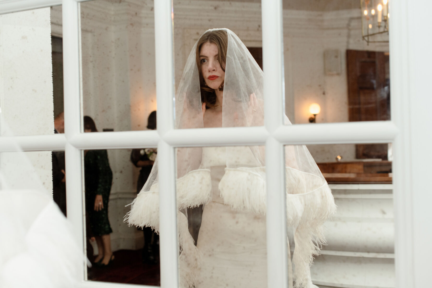 Bride looking into a mirror, wearing a Christopher Kane feather wedding veil.
