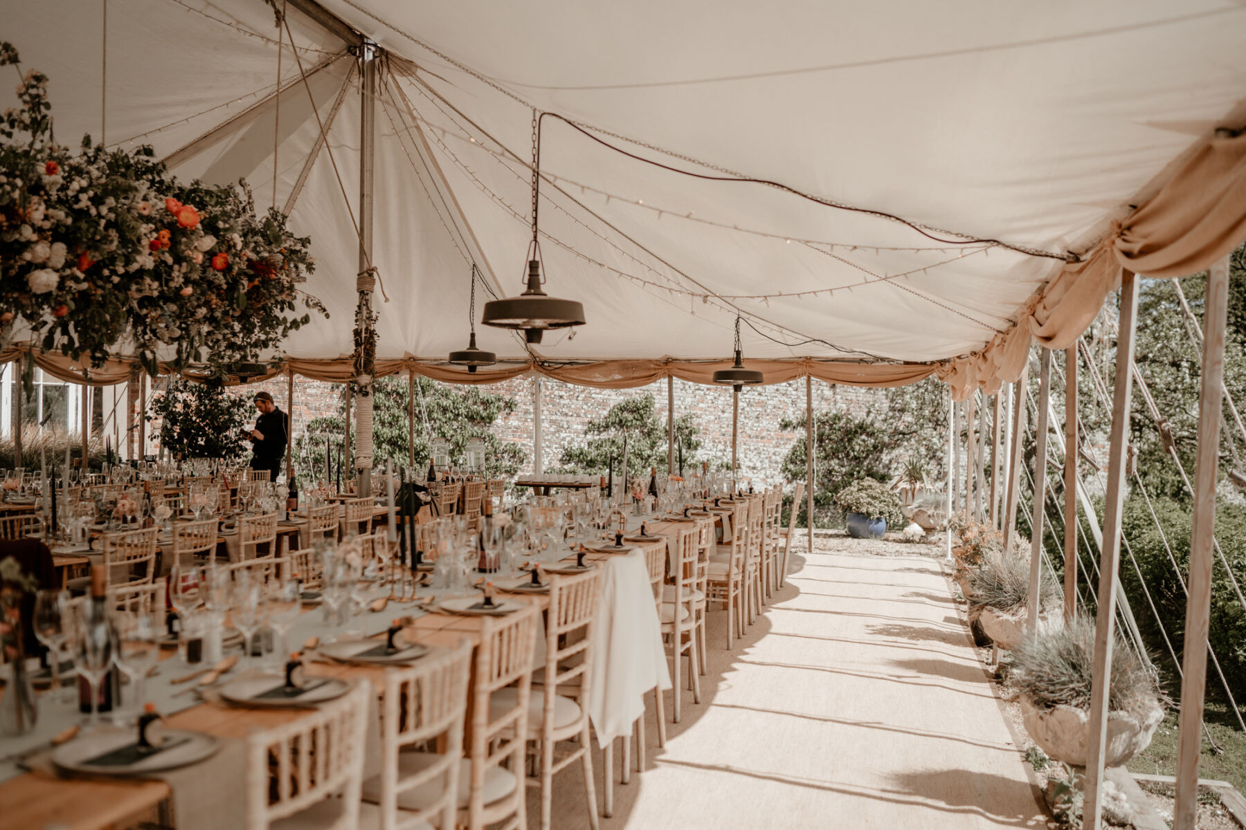 Elegant wedding marquee reception with long wooden tables and hanging flowers