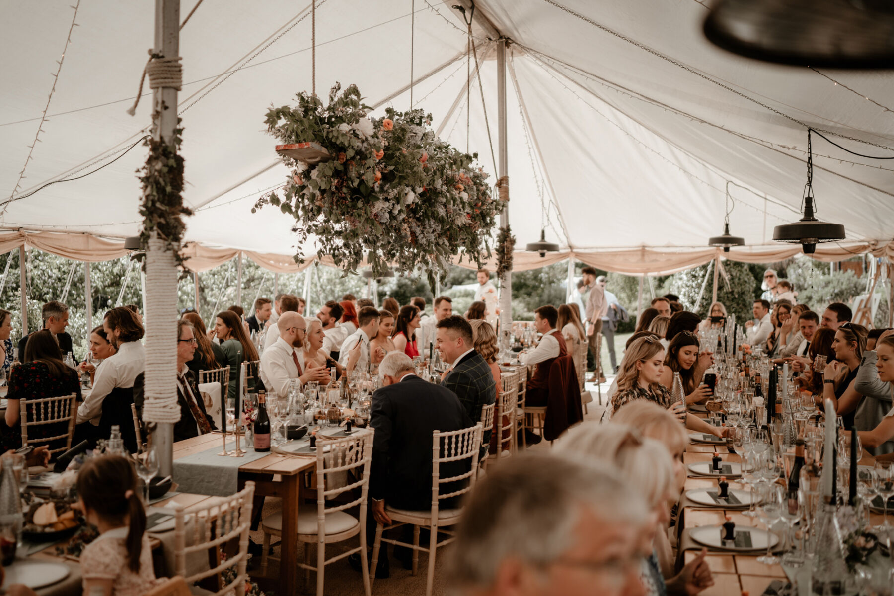 Marqee wedding reception with long wooden tables and hanging flowers