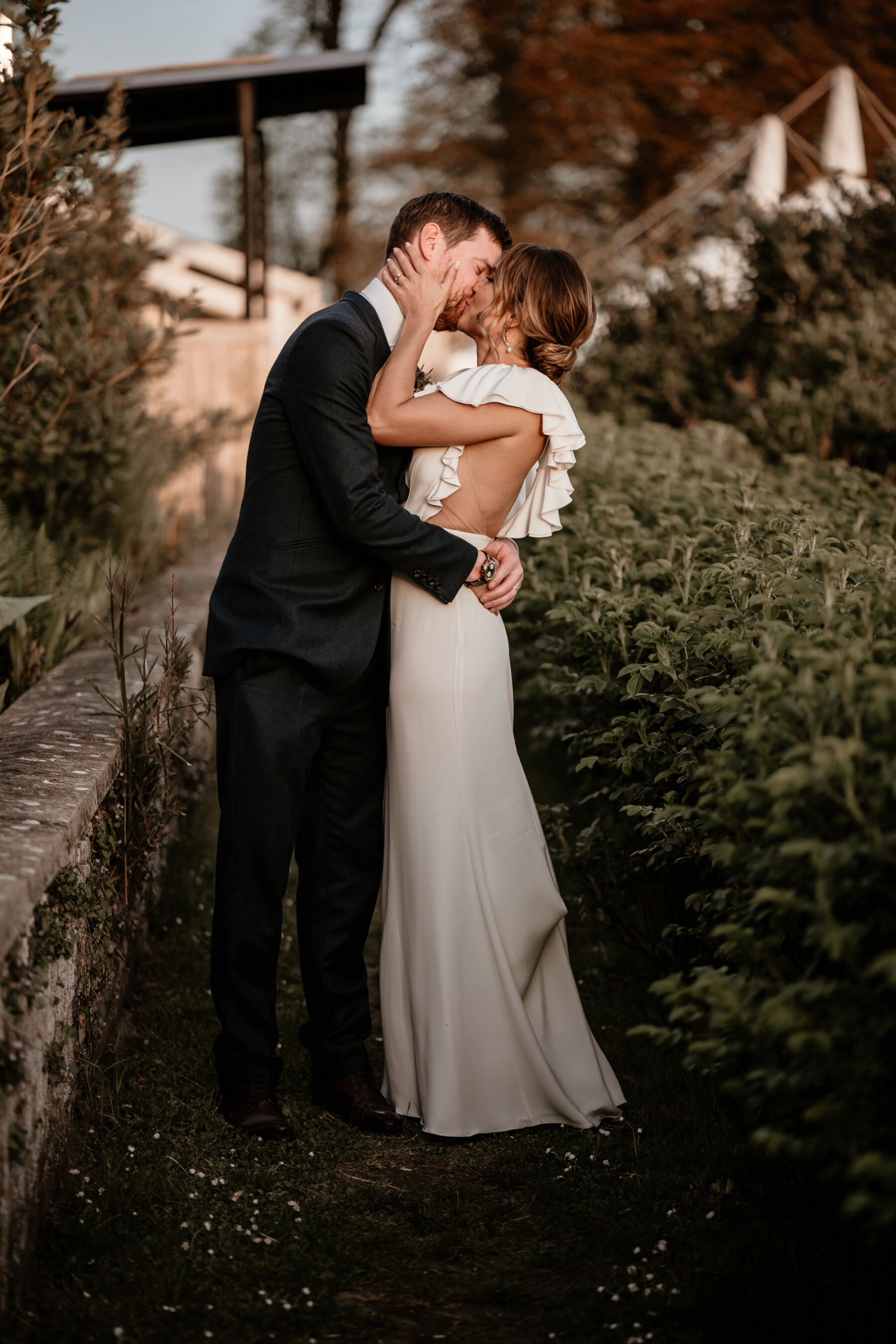 Bride and groom kissing and embracing. Alexandra Grecco ruffle sleeved wedding dress