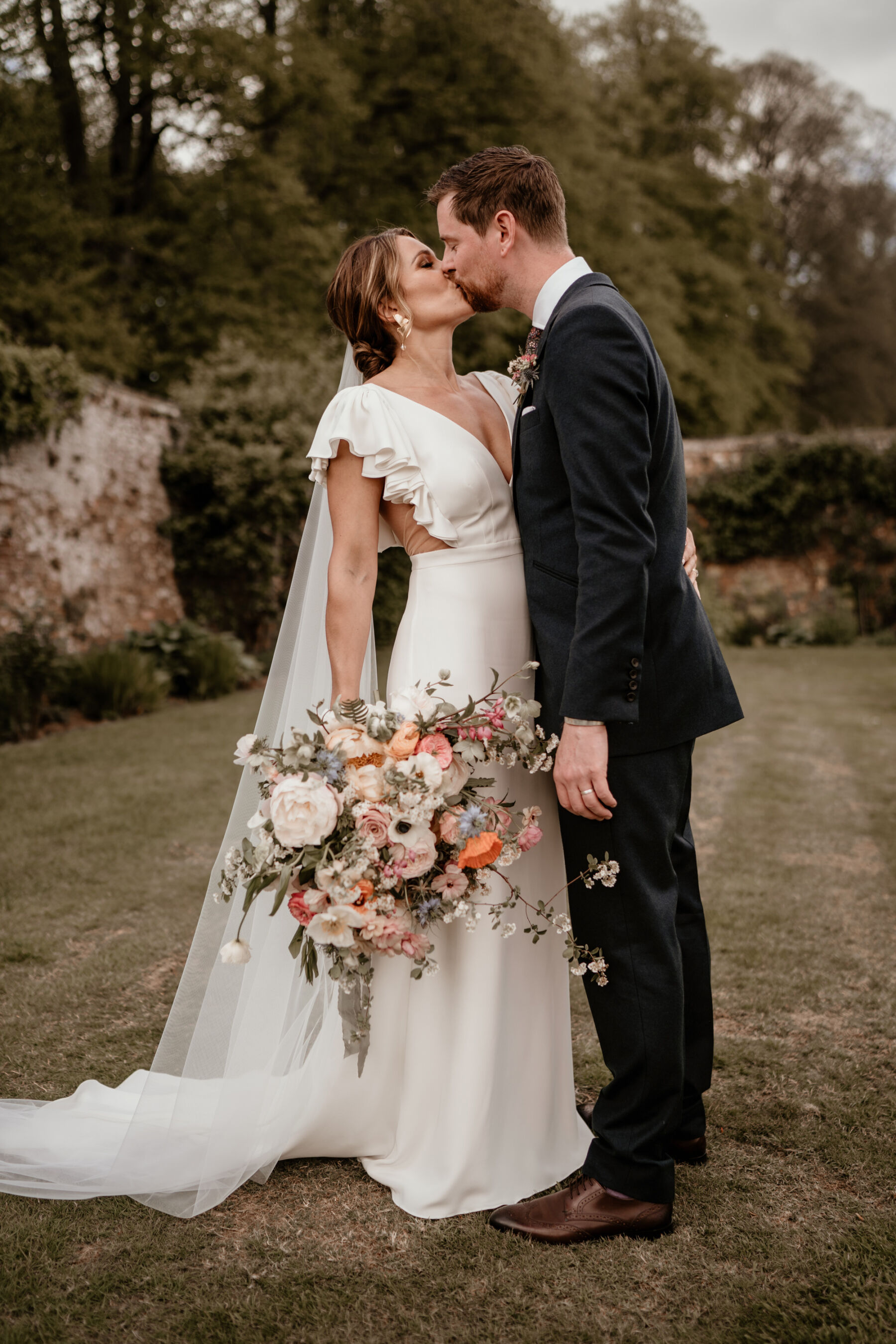 Bride and groom kissing and embracing. Alexandra Grecco ruffle sleeved wedding dress
