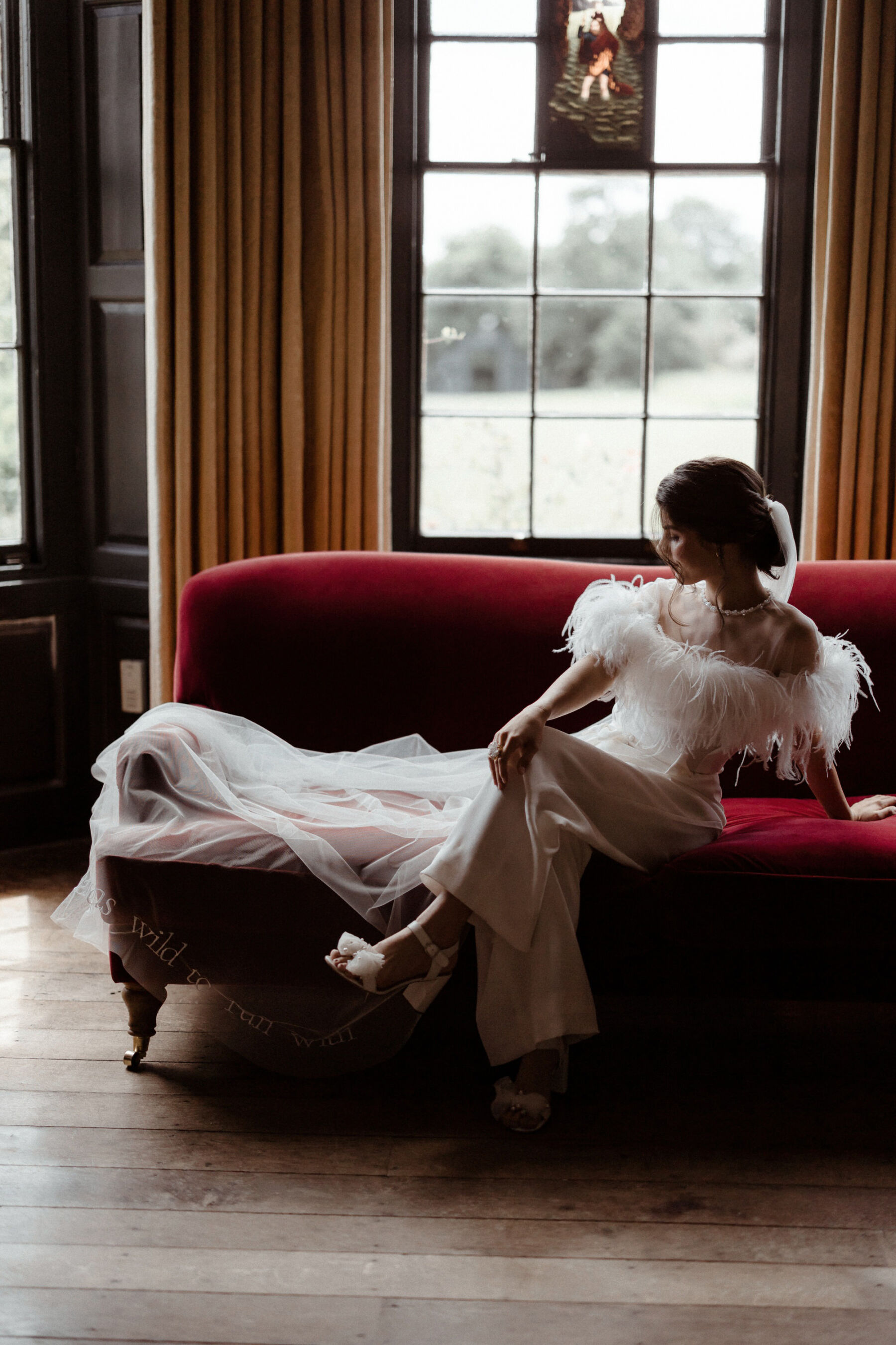 Bride reclining on a sofa at Elmore Court wearing an Ostrich feather top and trousers by Wilden London.