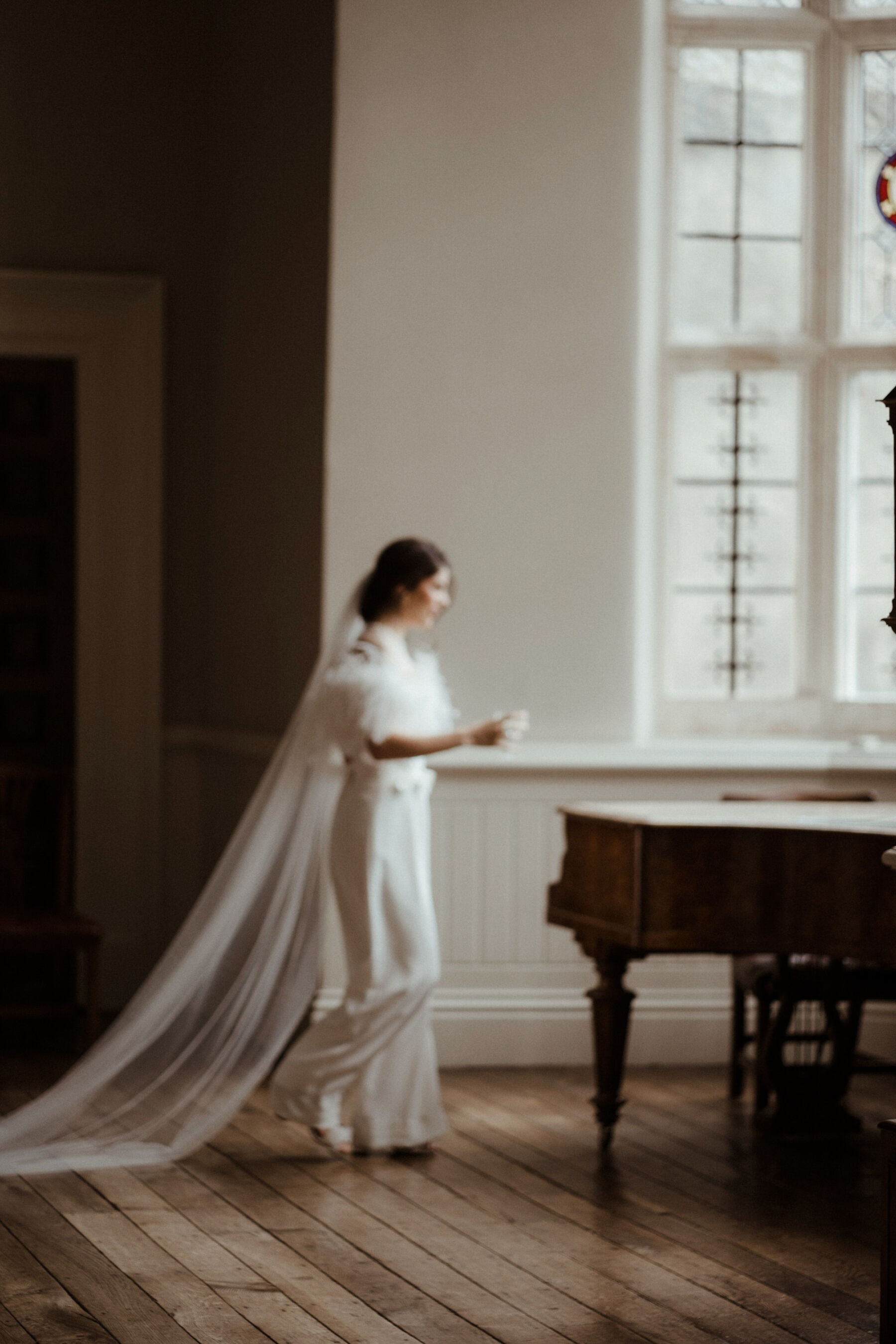 Bride walking past the grand piano in the drawing room at Elmore Court.