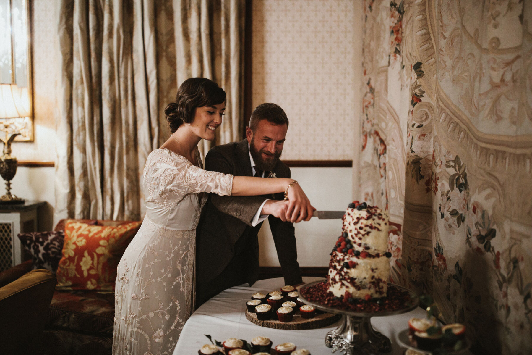 1920s inspired bride in vintage wedding dress cutting the wedding cake.