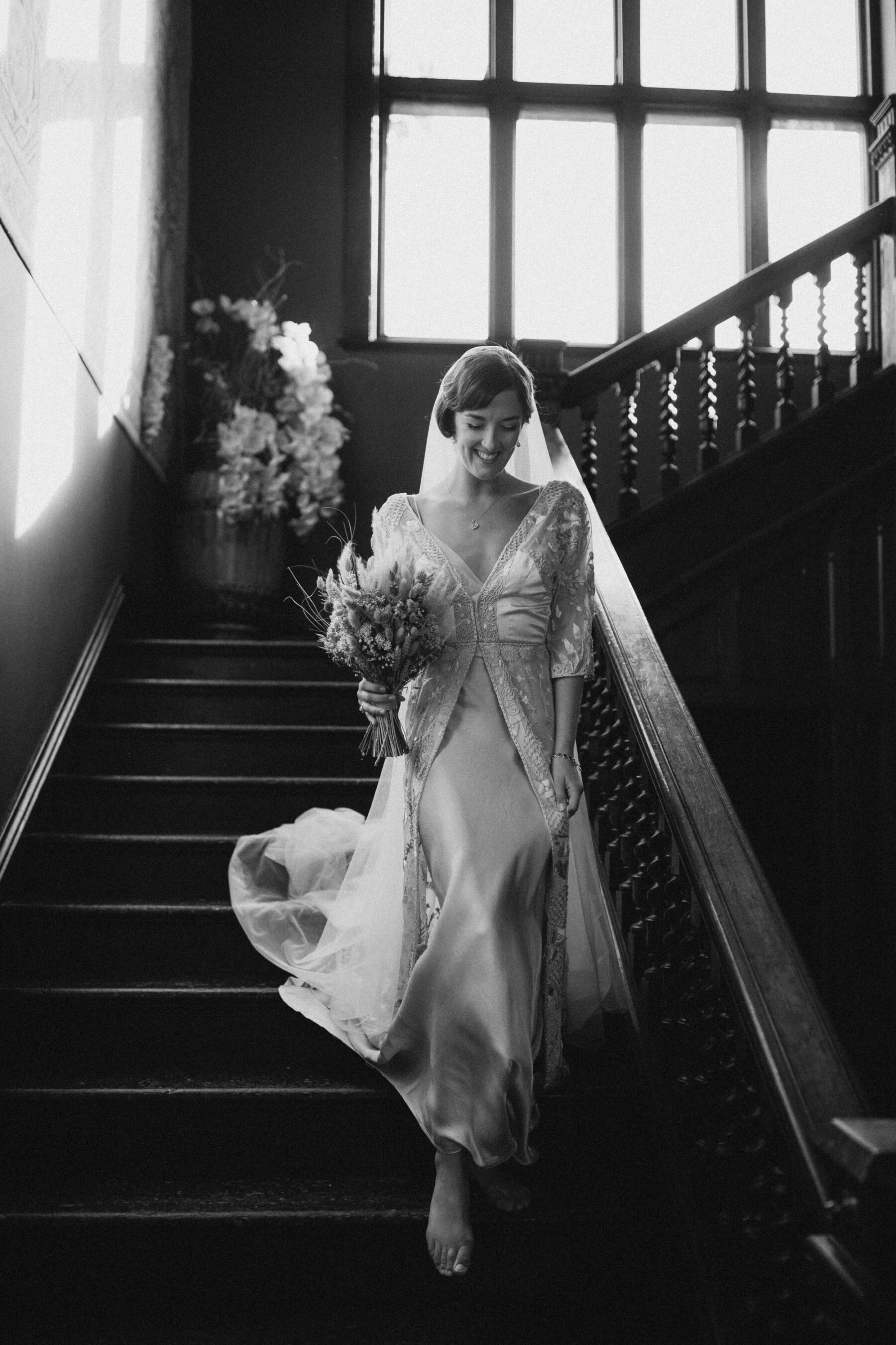 Barefoot bride walking down the stairs at Huntsham Court in Devon. She wears a vintage wedding dress by Jane Bourvis.