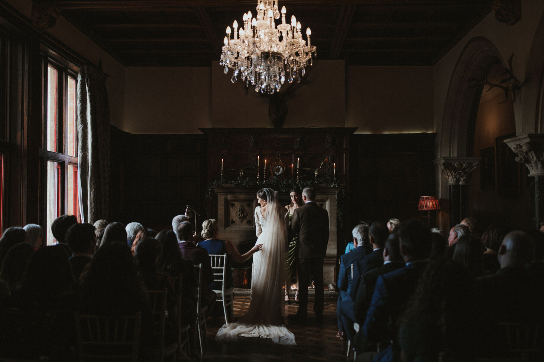 Bride and groom with their backs to the camera during their wedding cermeony at Huntsham Court, Devon. Bride wears a long cathedral length veil.