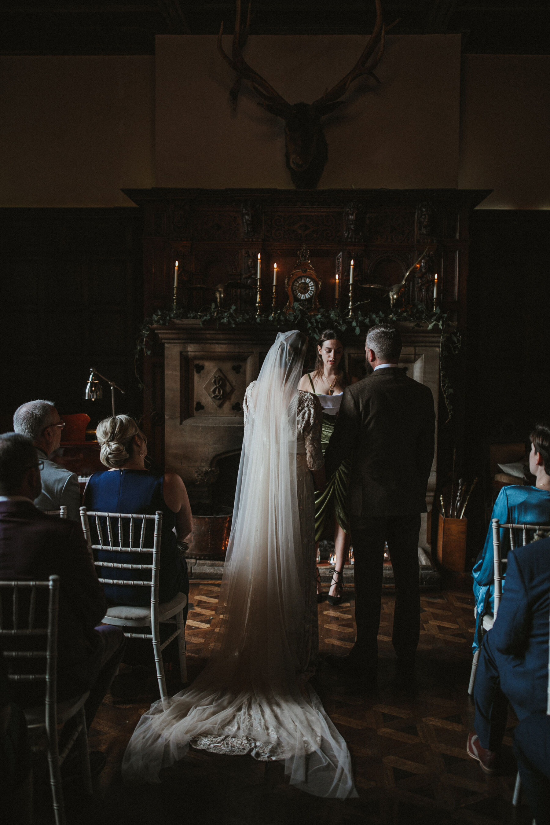 Bride and groom with their backs to the camera during their wedding cermeony at Huntsham Court, Devon. Bride wears a long cathedral length veil.