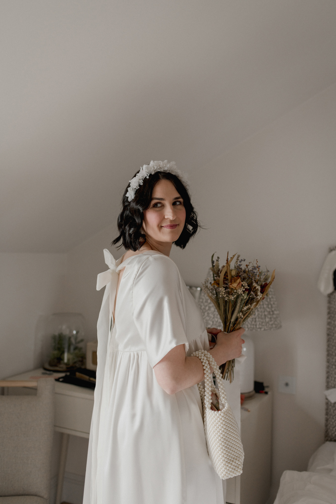 Modern wedding dress with bow at back. Bride carries a dried flower wedding bouquet.