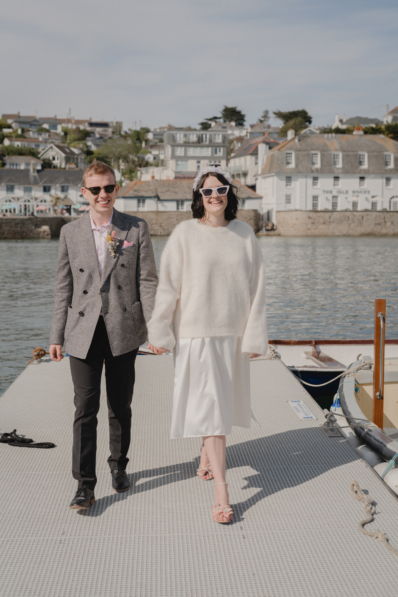 Bride in sunglasses, white jumper and mid length dress. Cornwall wedding.