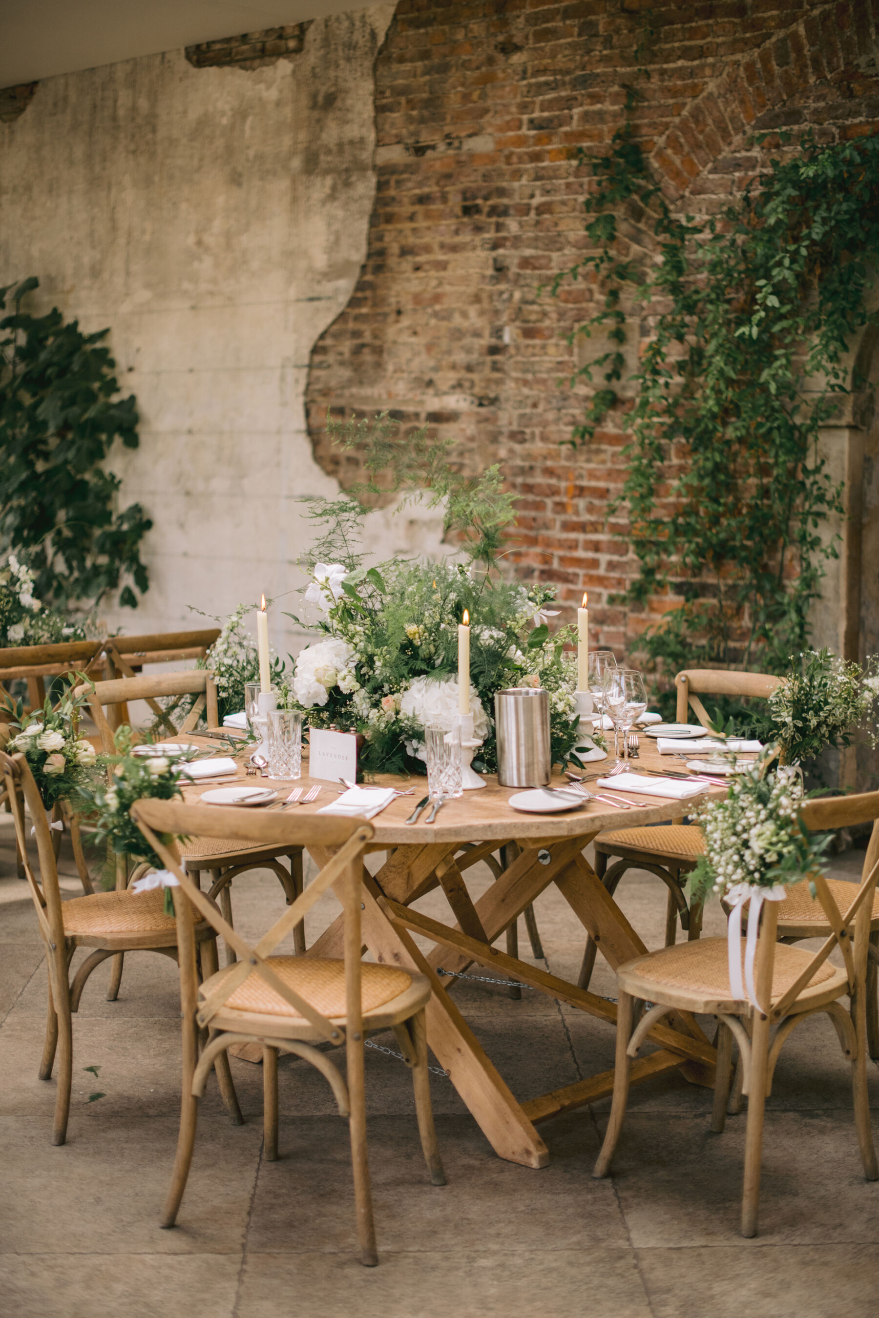 Elegant pared back wedding table decor with seasonal summer flowers and greenery. Wooden crossback chairs.