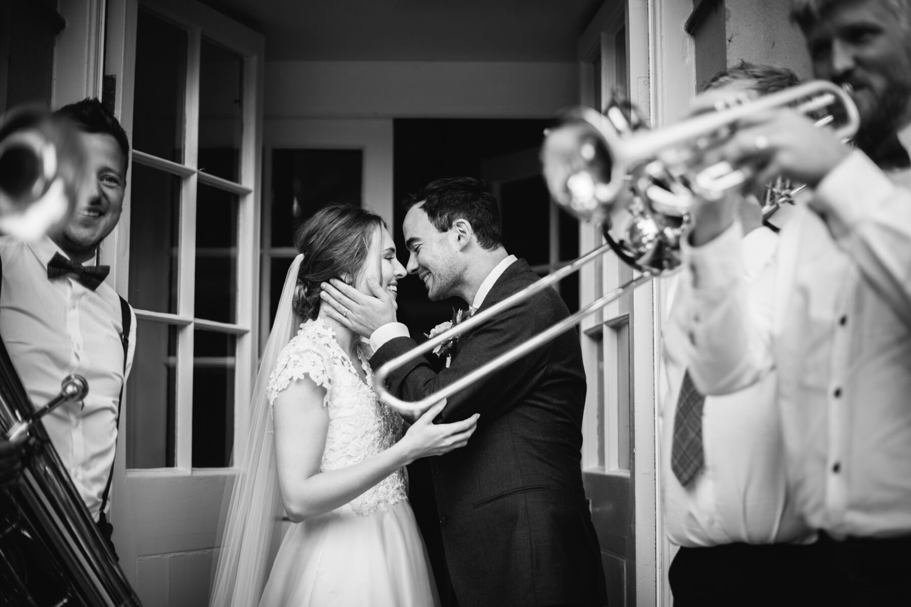 Groom lovingly holding bride's face as a brass band serenade them.