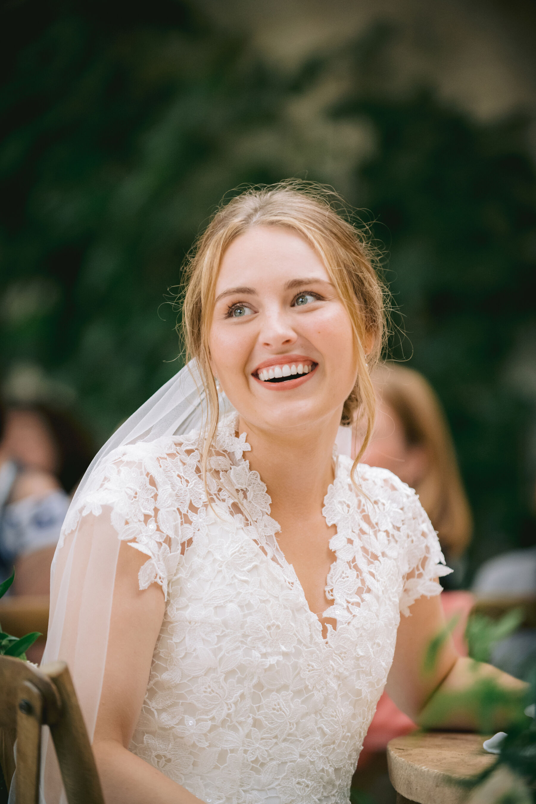 Bride smiling as she watches groom giving a speech.