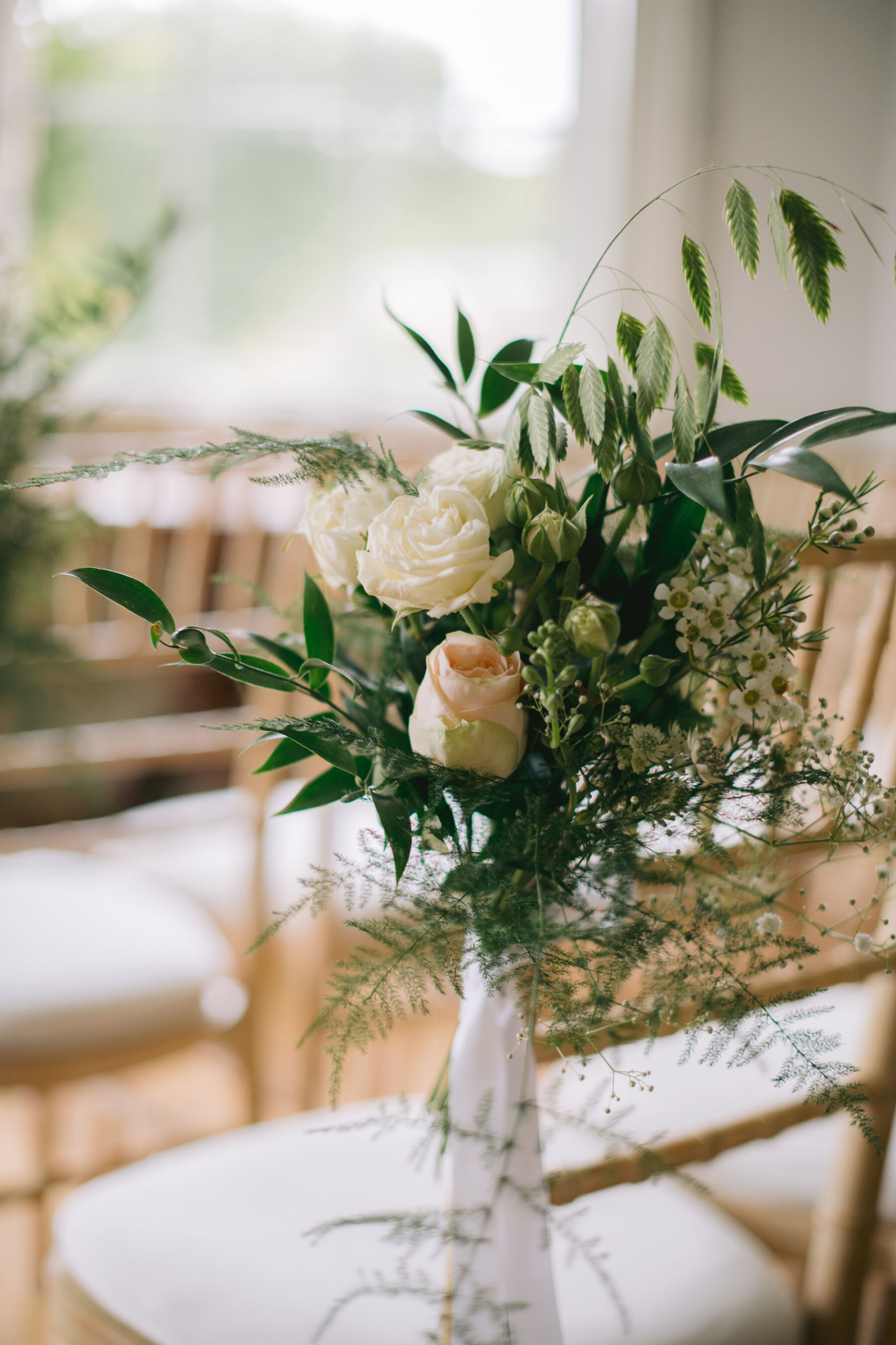 Simple seasonal summer wedding flowers tied to a chair at the end of the aisle.