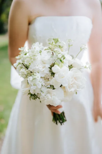 A close up image of an all white bridal bouquet. It's being held by the bride.