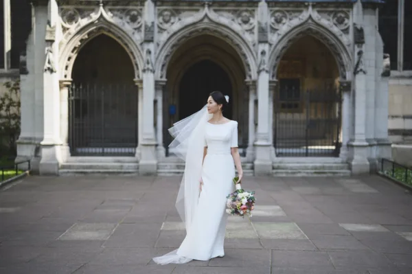 A bride stands outside St Margarets Church, Westminster Abbey holding her bouquet.