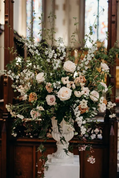 A large garden urn sits on a pedestal in St Mathias Church, Richmond. Full of Spring foliages, blossom and roses. In pale ivory and toffee colours.