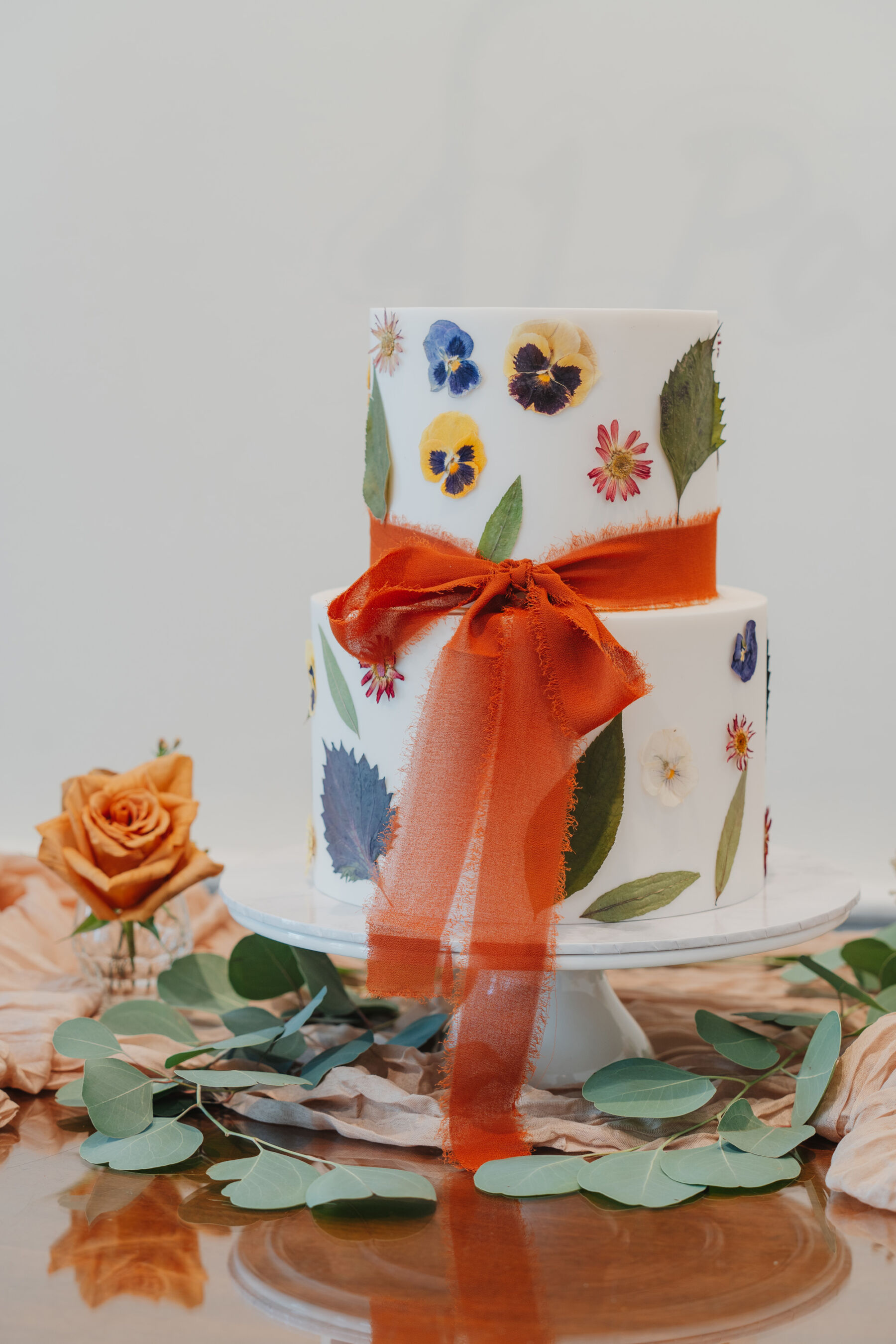 Wedding cake with pressed flowers and orange silk ribbon.