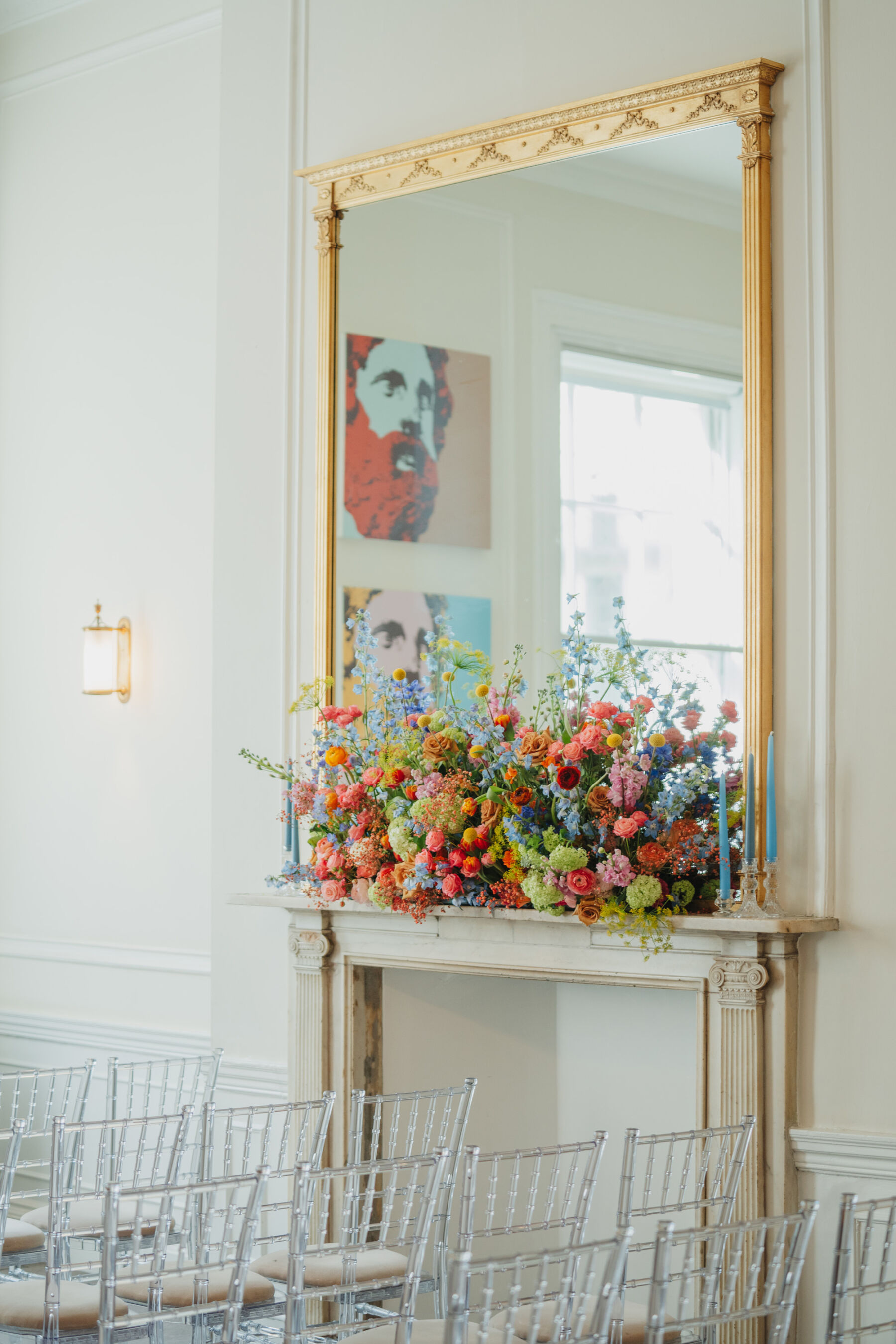 Mantelpiece at 41 Portland Place with a gold framed mirror on top and decorated with bright and colourful sustainable wedding flowers.