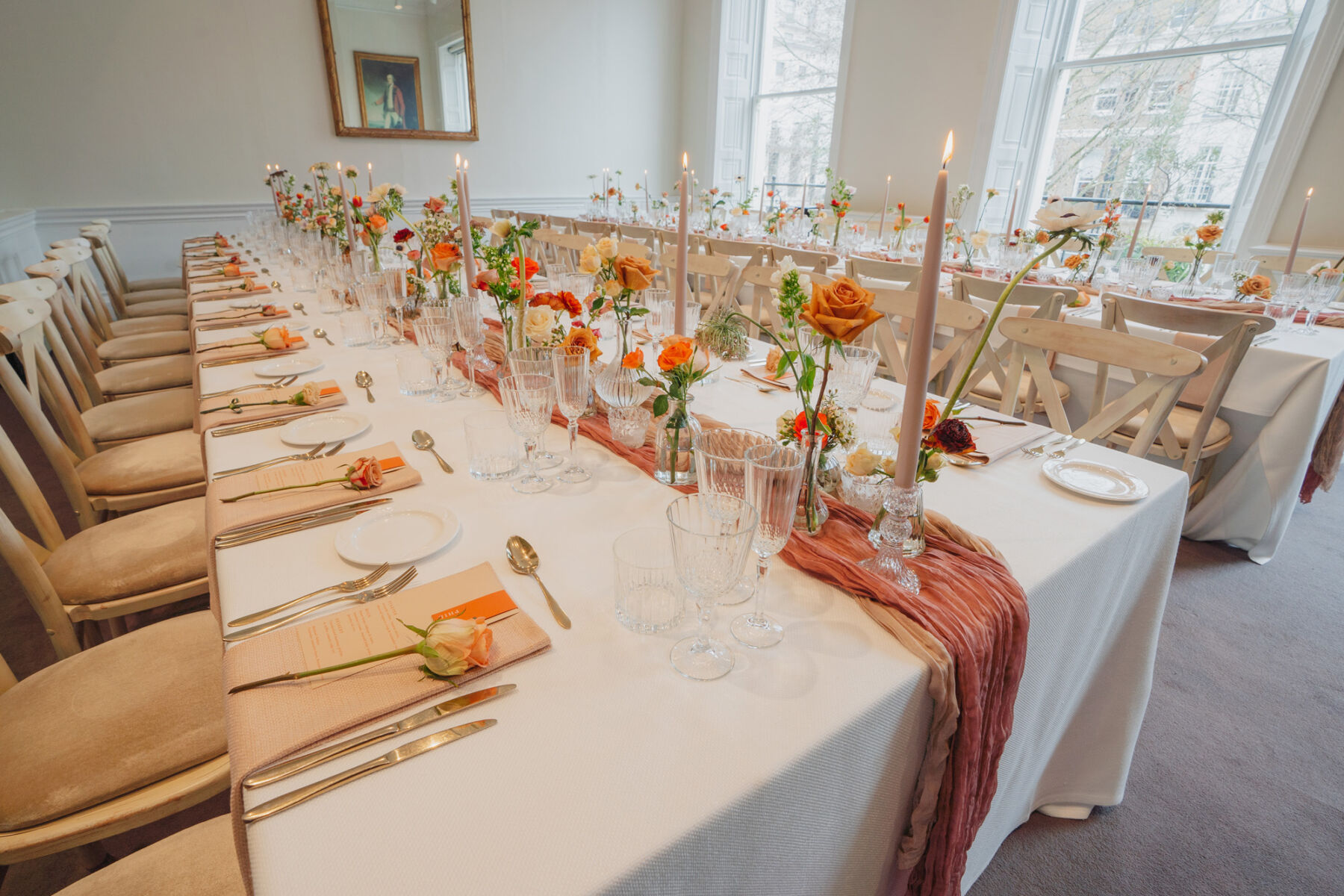 Elegant orange and cream wedding flowers in bud vases surrounded by rubbed glasses, taper candles and hand dyed table runners.