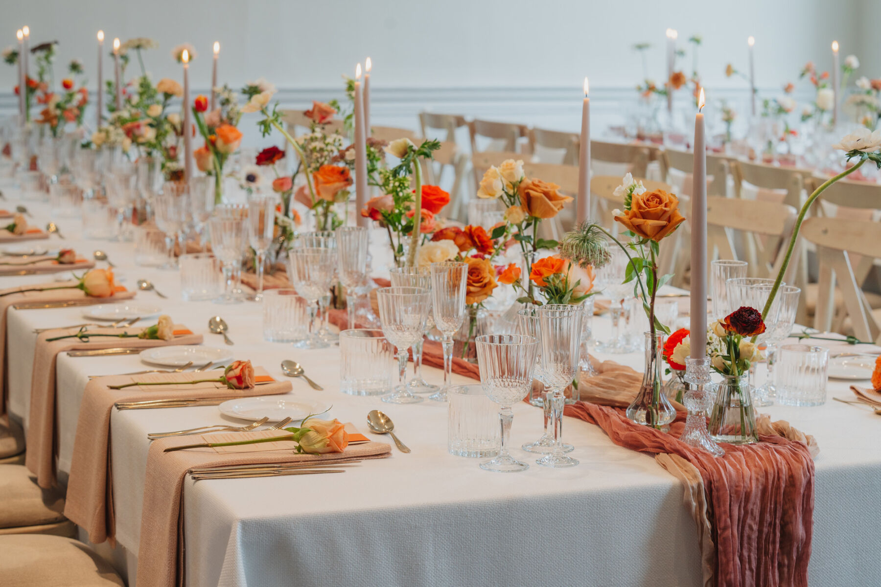 Ribbed glasses and elegant taper candles. Hand dyed table runners in natural shades. Orange and cream roses.