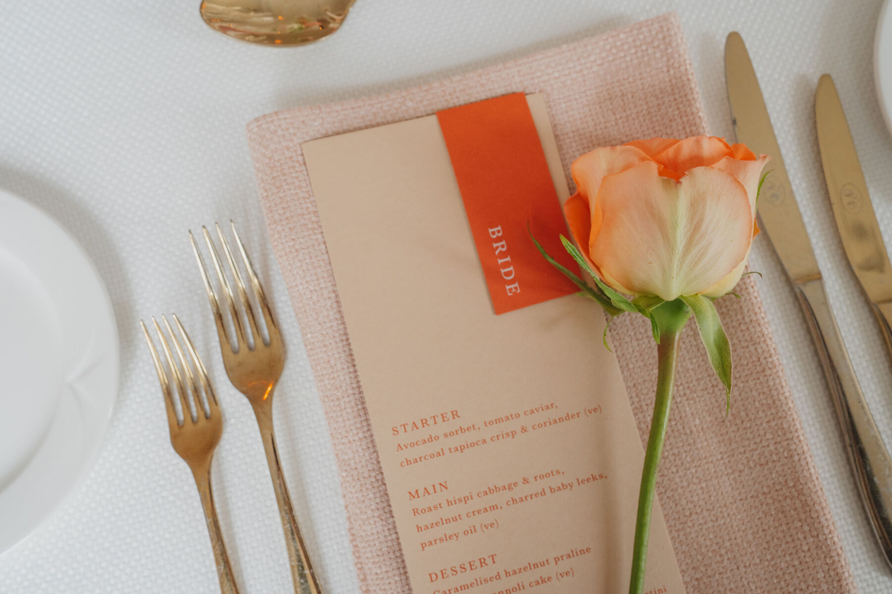 Elegant pale orange wedding menu and single stem rose and gold cutlery.