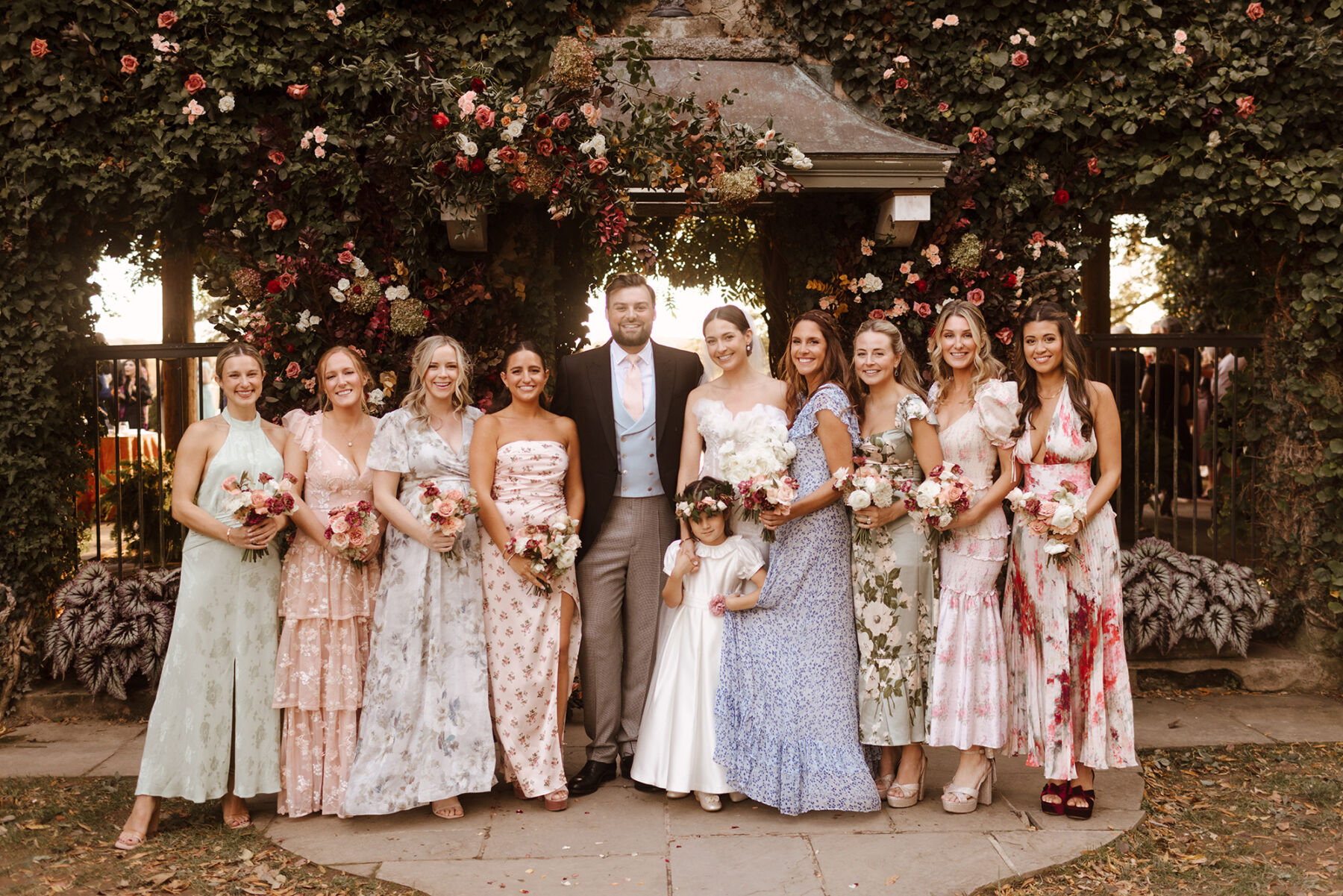 Bride and groom standing with bridesmaids in pretty pastel mismatched dresses.