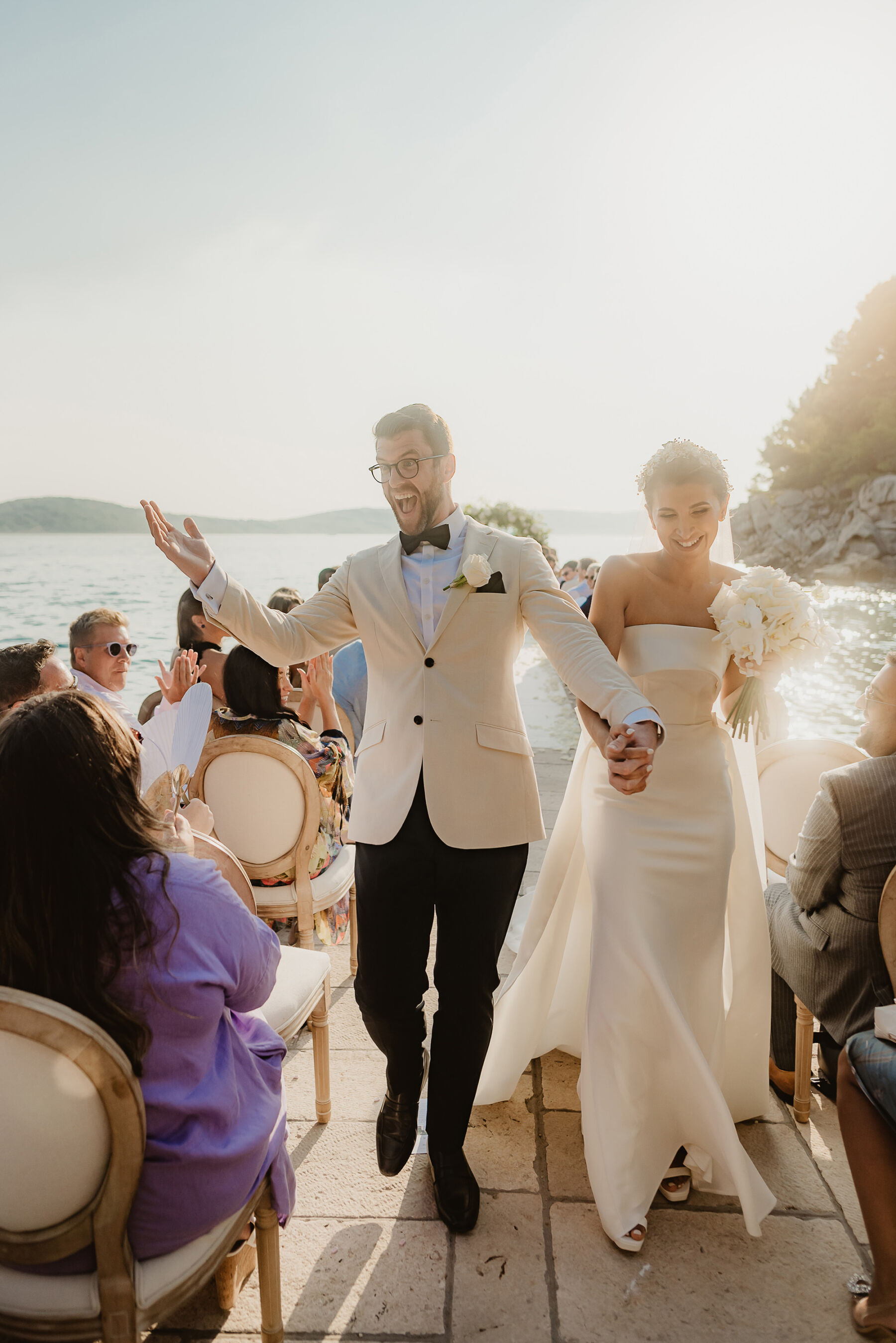 Joyful groom in white tux, outdoor wedding by the sea 