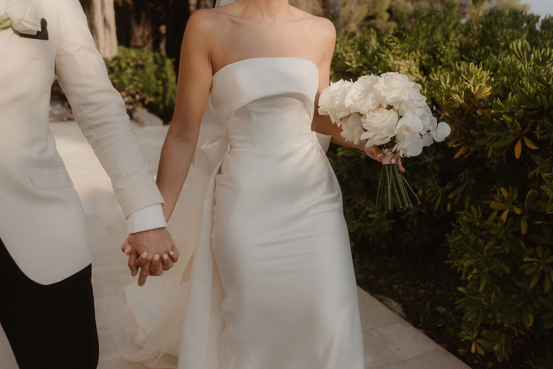 Bride with white nail varnish holding hands with groom in white tuxedo. Bride wears Eva Lendel wedding dress.