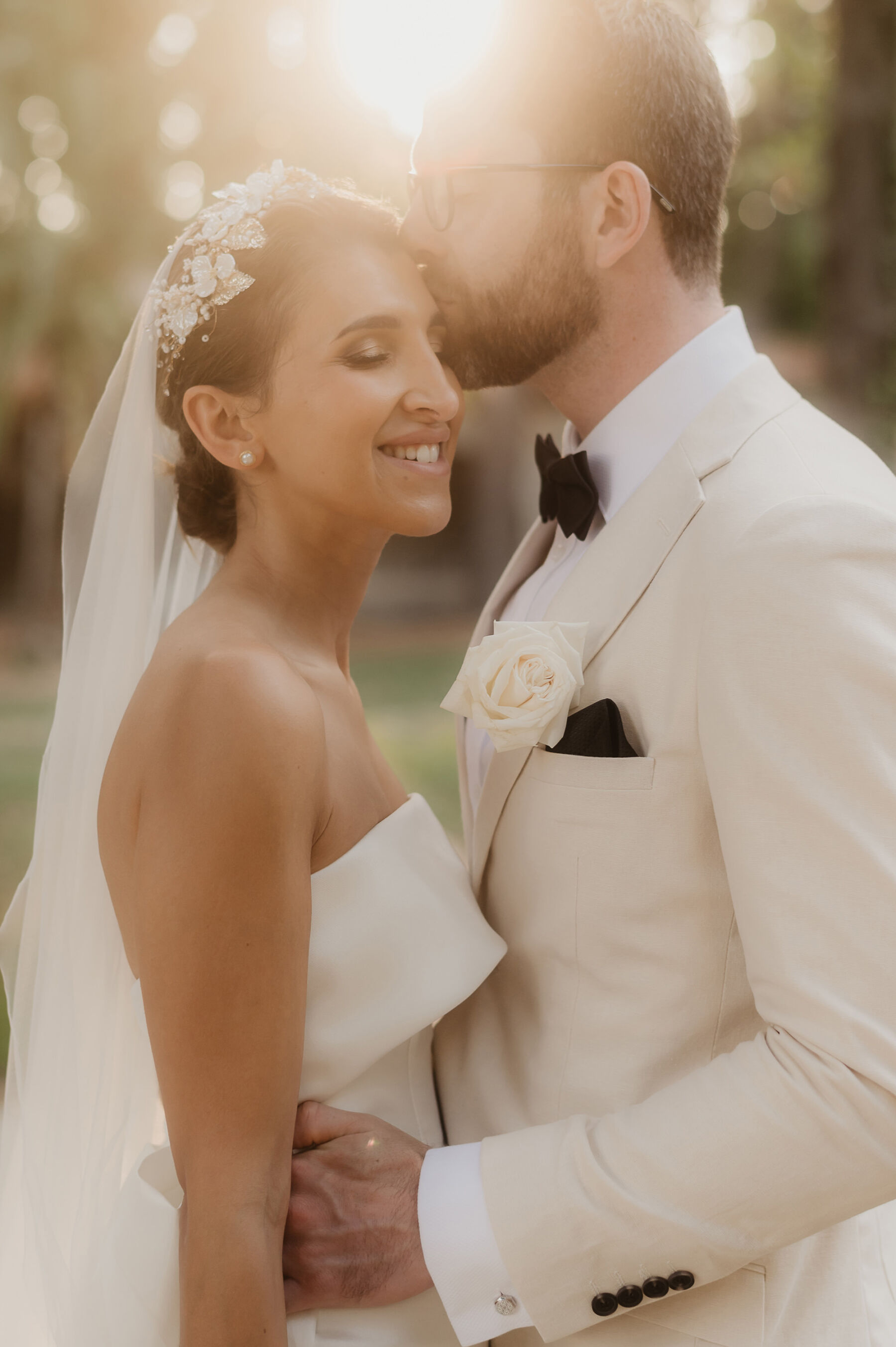 Groom in white tux kissing bride in minimalist wedding dress by Eva Lendel